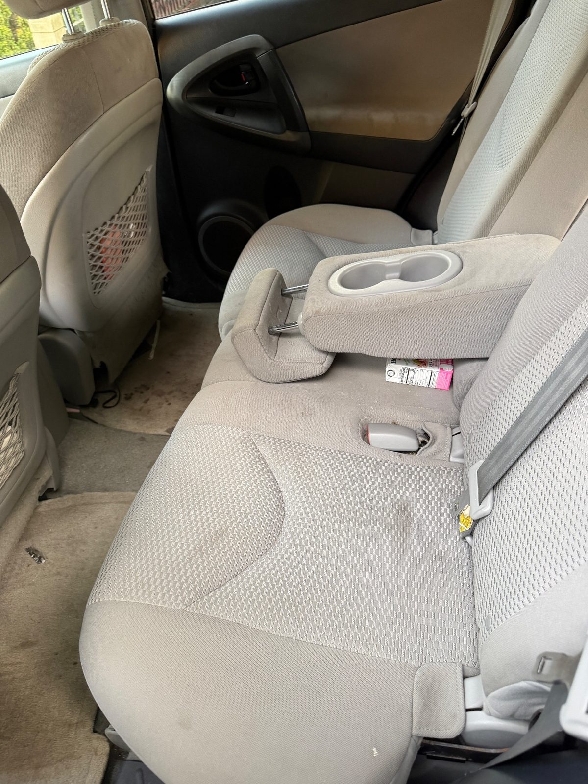 Rear bench of a 2011 Toyota RAV4 before detailing, stained cushion and a juice box in the seat gap