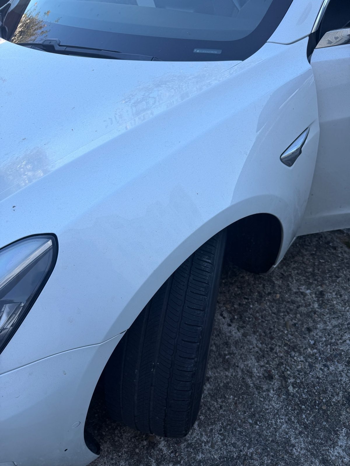 Front fender of a white Tesla Model 3 before detailing, with a dusty film and water spots