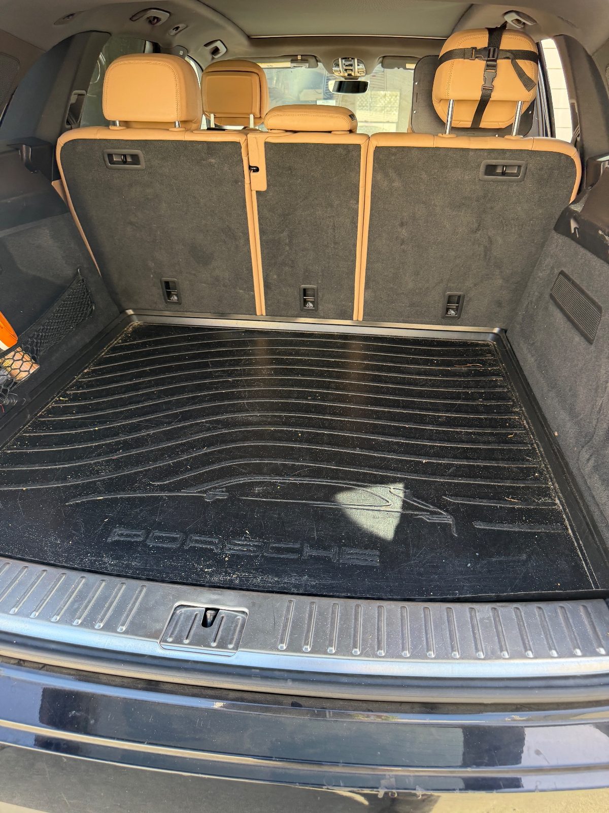 Cargo area of a dark blue Porsche Cayenne before detailing, rubber mat covered in dust and crumbs