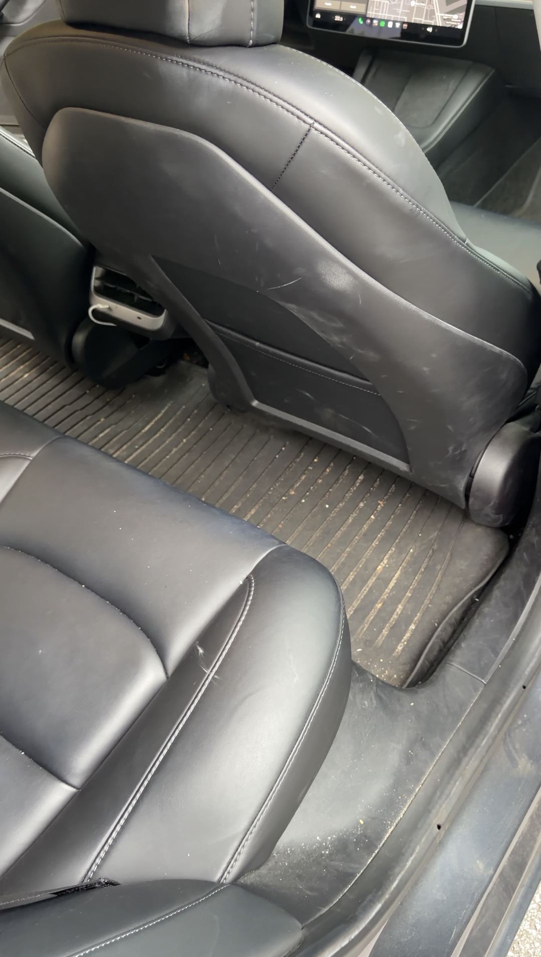 Rear passenger-side footwell of a Tesla Model 3 before cleaning, dusty mat and scuffed seat back