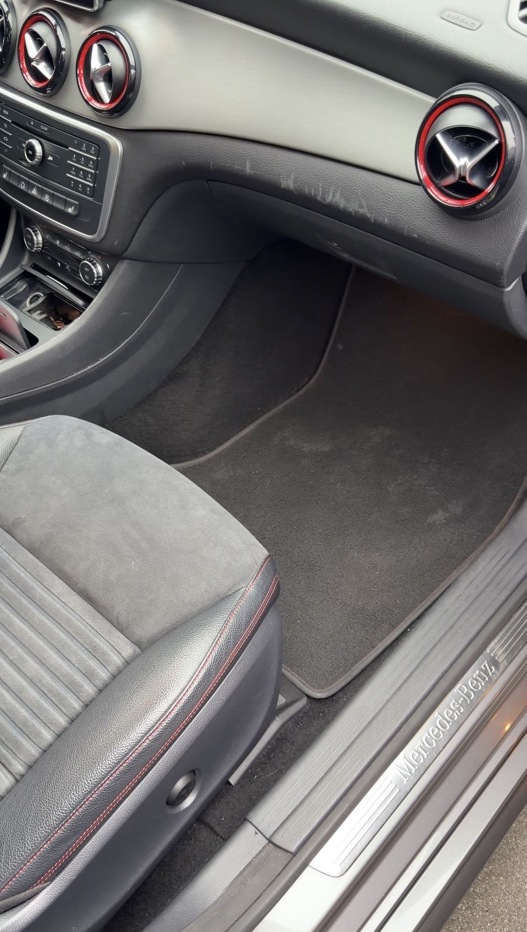 Dirty front passenger footwell of a grey Mercedes-Benz CLA250 before detailing, with a chalky pale deposit across the carpet mat