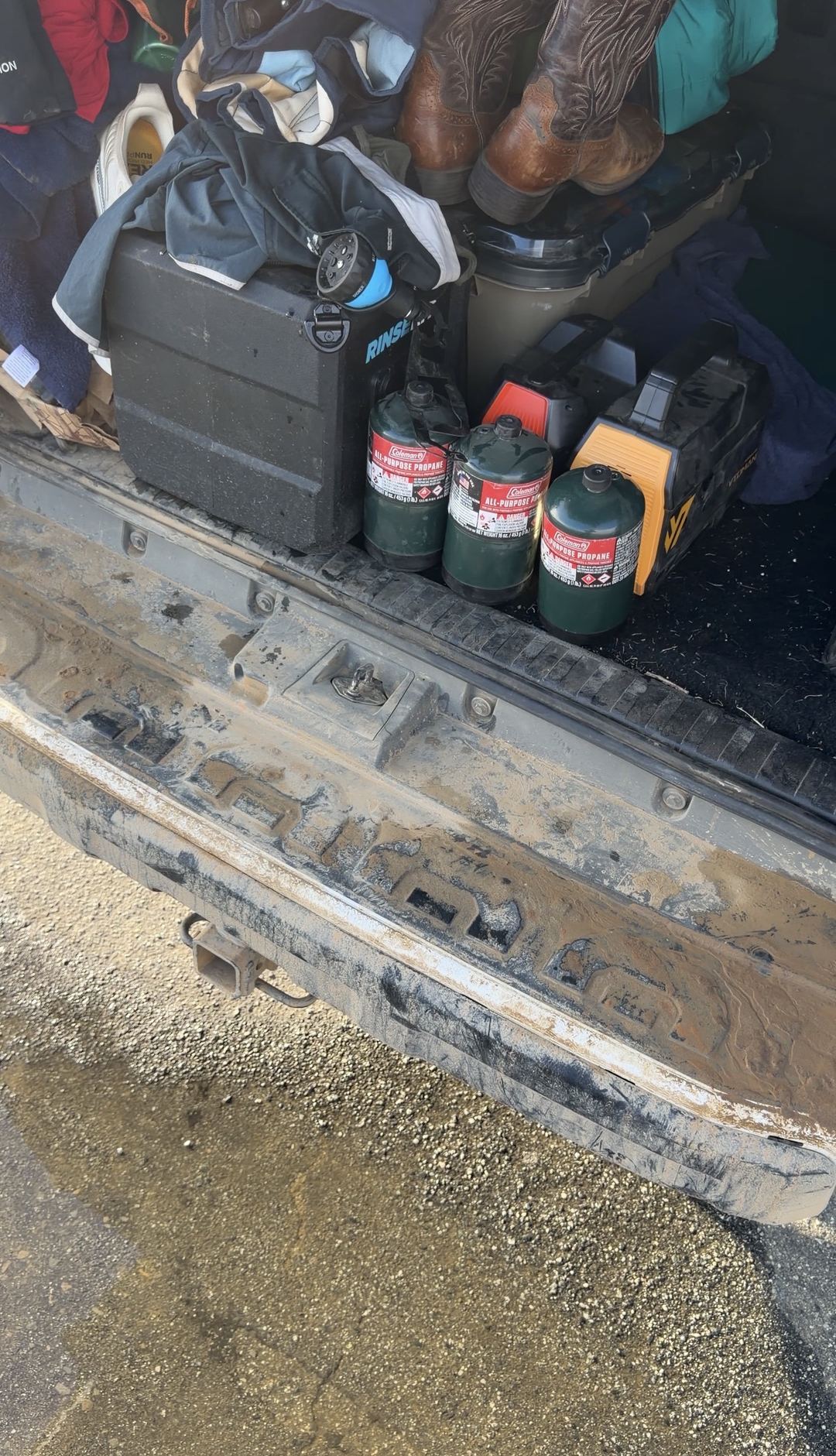 Mud-caked rear bumper step of a Toyota 4Runner with propane canisters and camping gear in the cargo area