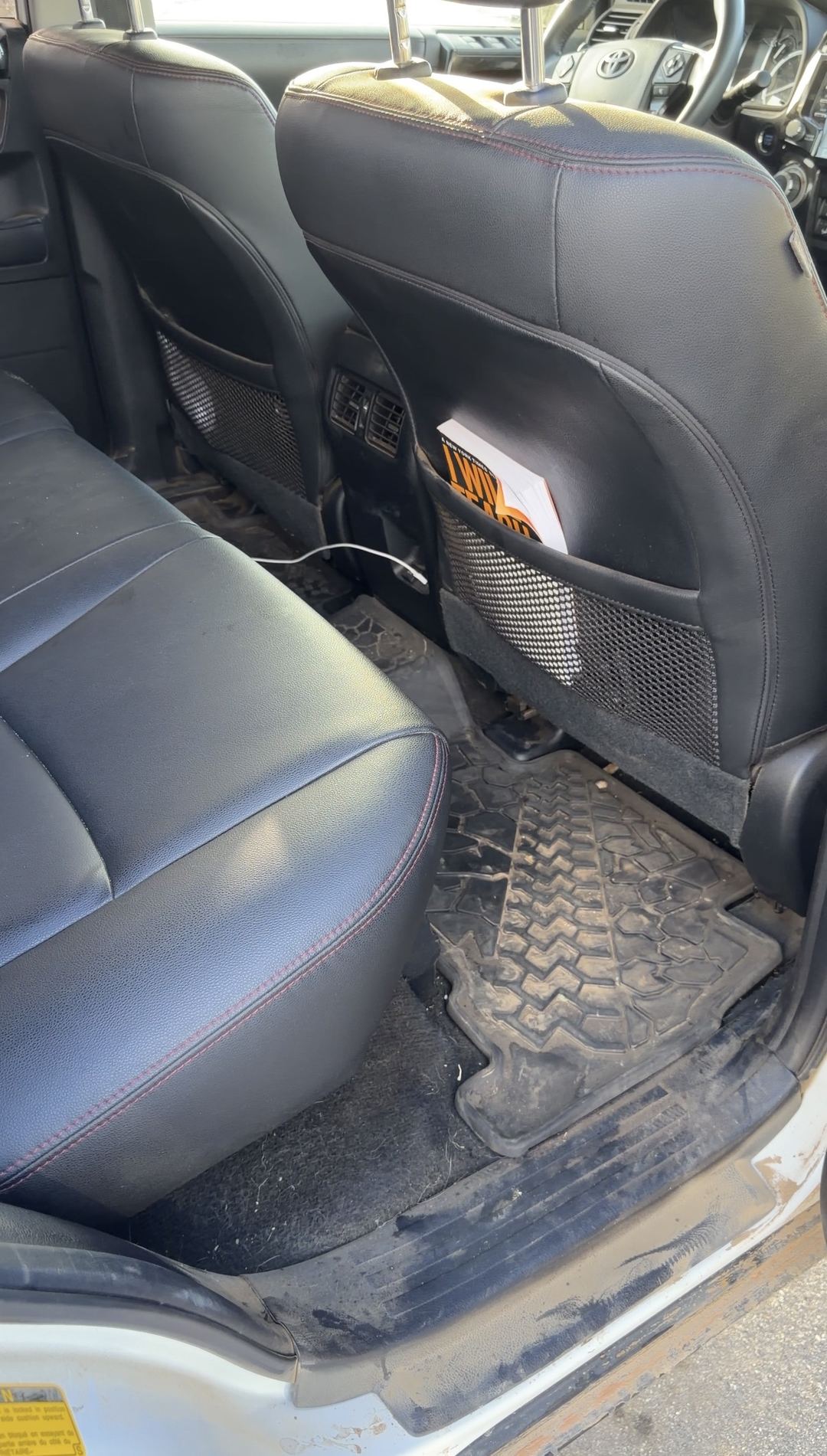 Rear passenger footwell of a white Toyota 4Runner with dried dirt on a tread-pattern mat and a muddy door sill