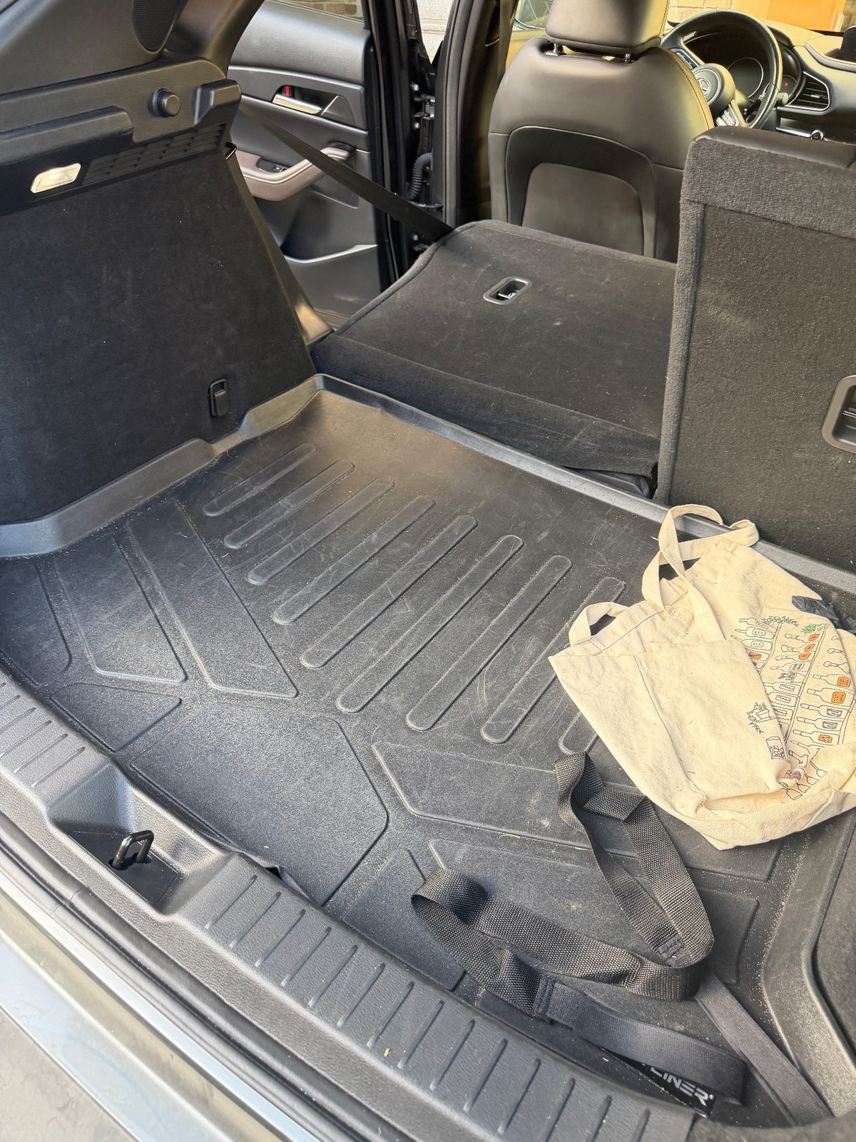 Left side of the cargo area of a grey Mazda CX-30 before cleaning, dusty liner with a tote bag