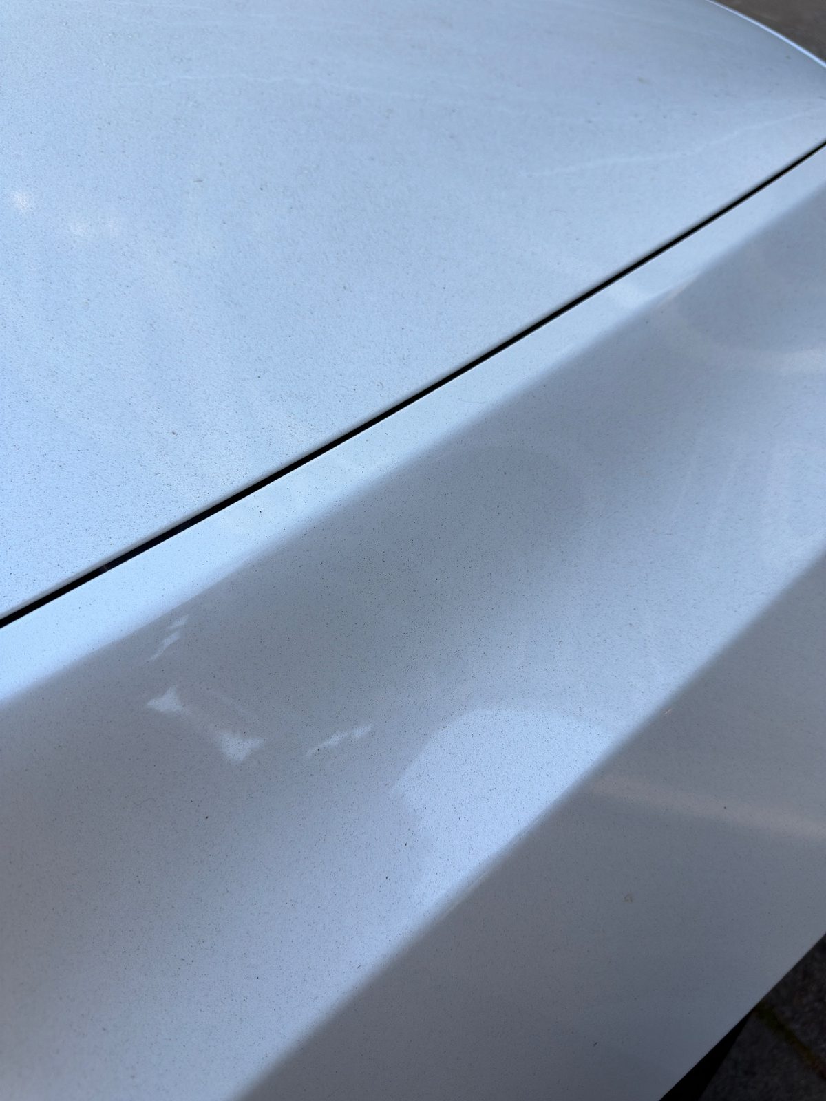 Close-up of dusty white Tesla Model Y bonnet and fender before detailing
