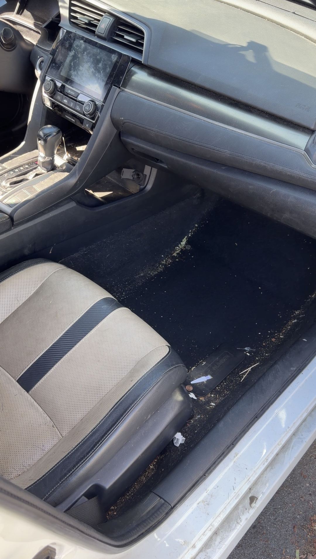 Passenger footwell of a Honda Civic before cleaning, carpet covered in grit, wood fragments and paper scraps