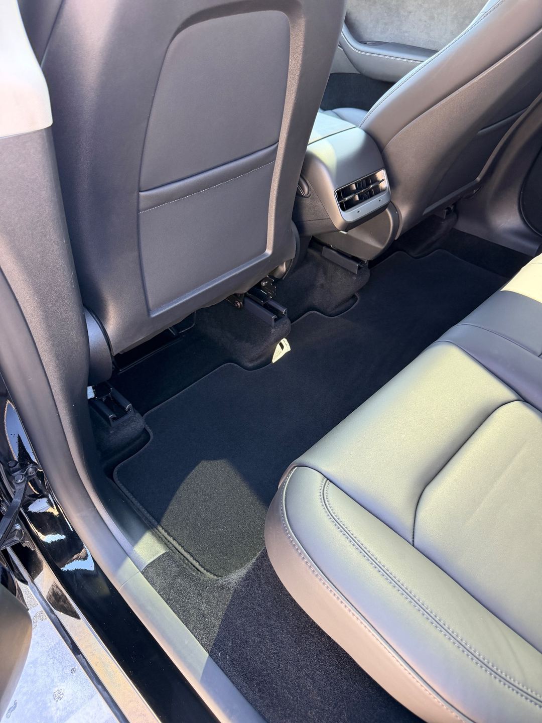 Rear footwell of a black Tesla Model Y after detailing, the floor mat vacuumed clean
