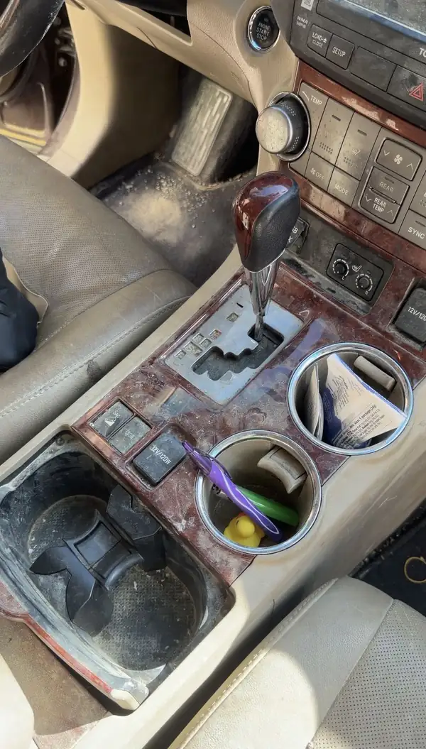 Dusty wood-grain centre console and cluttered cupholders in a Toyota Highlander before cleaning
