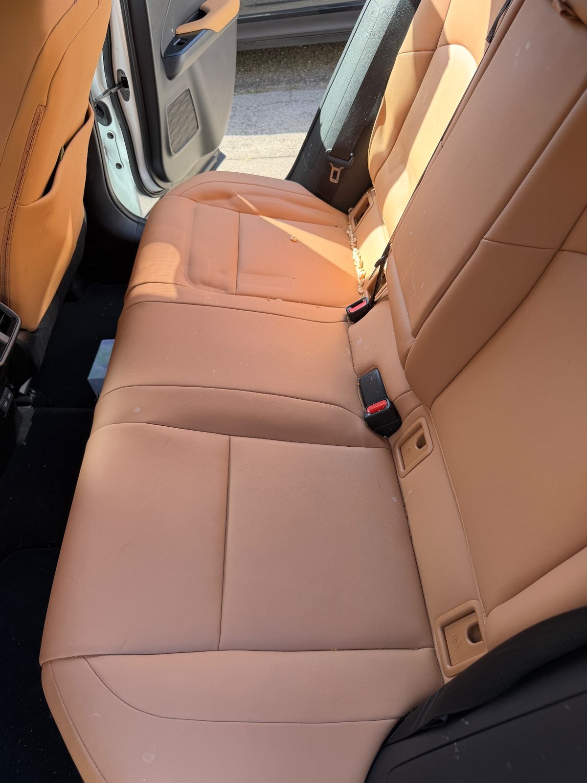 Rear bench seat of a white Lexus UX before detailing with crumbs in the crease and spots on the leather