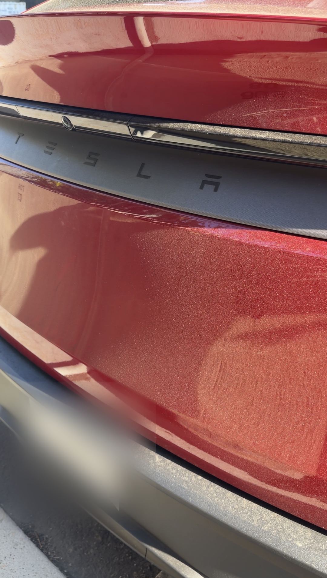 Dust-covered red Tesla liftgate with visible wipe marks before an exterior detail