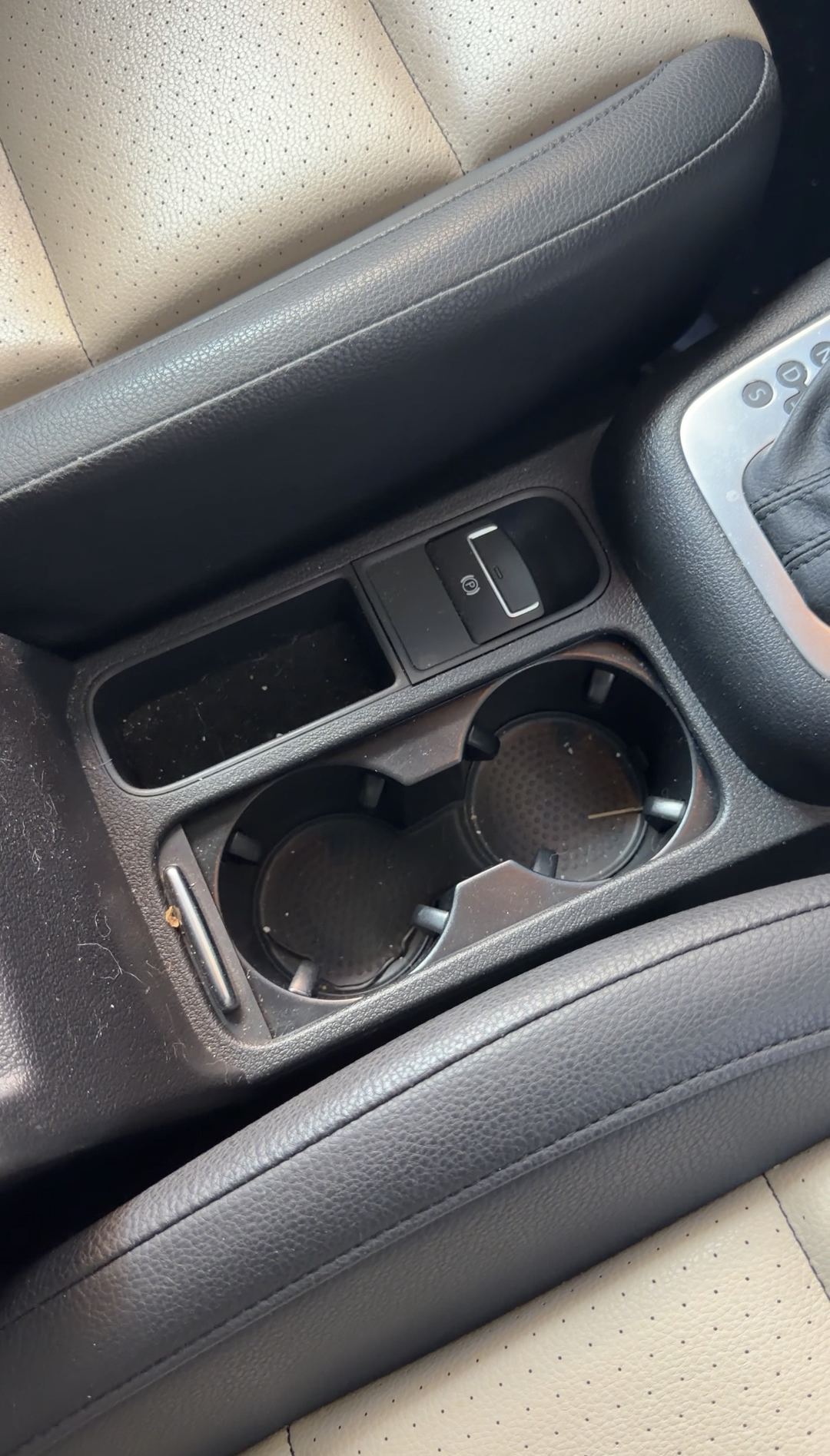 Centre console and cupholders of a VW Tiguan before detailing, with dust in the tray and a toothpick left in a cupholder.