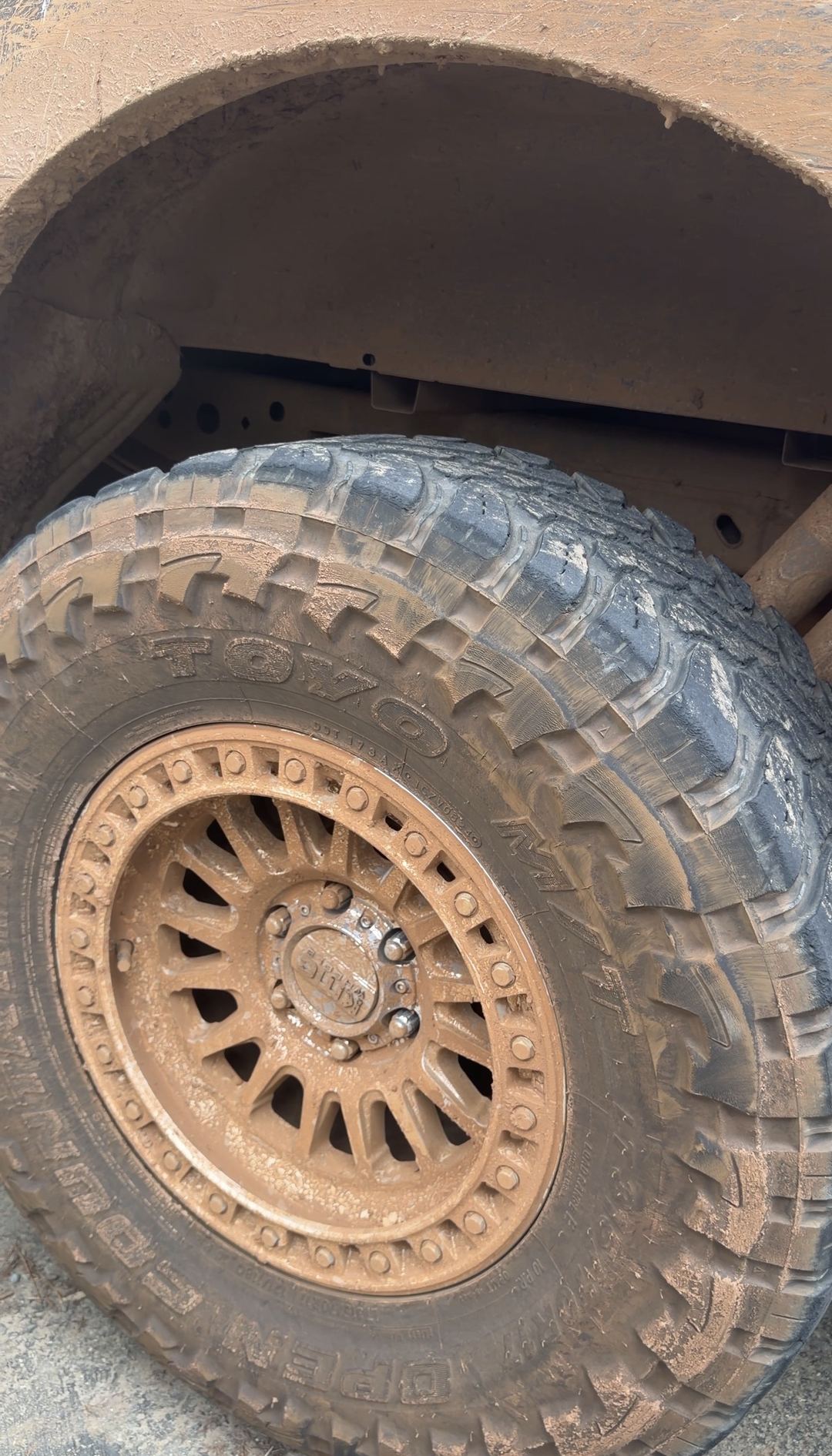 Wheel and mud-terrain tyre packed solid with dried mud before cleaning