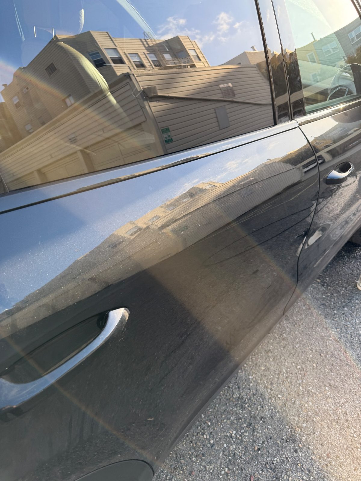 Rear door of a dark blue Porsche Cayenne before washing, dusty paint with building reflections