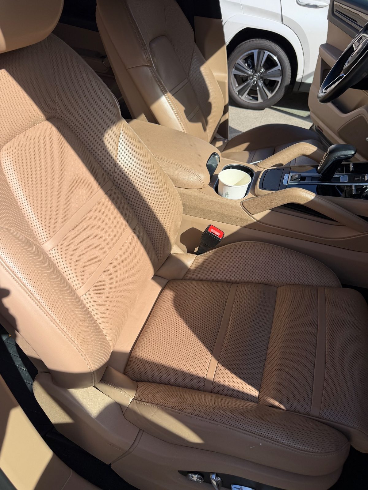 Front passenger seat of a dark blue Porsche Cayenne before cleaning, dusty leather and a cup in the cupholder
