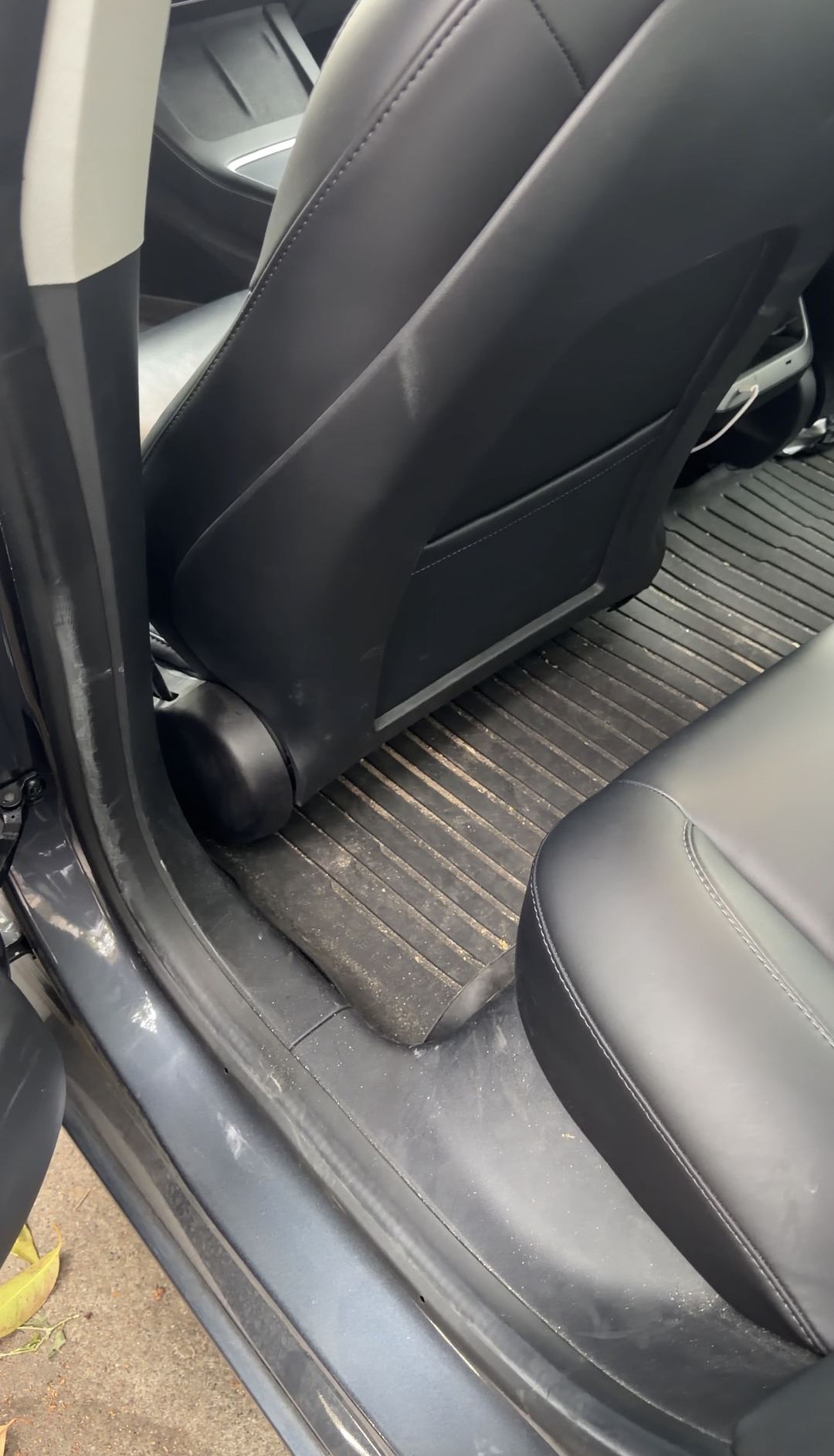 Rear footwell behind the driver seat of a Tesla Model 3 before cleaning, dirt in the mat ribs