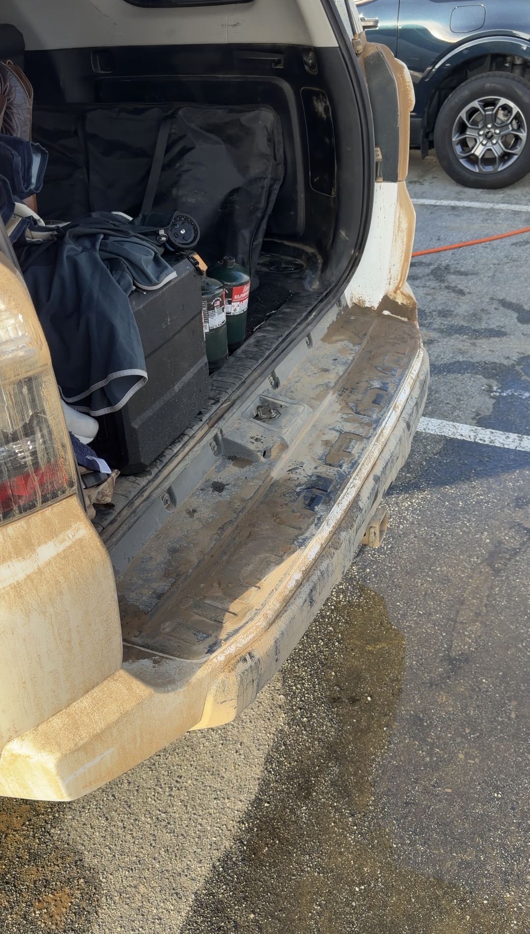 Open cargo area of a white Toyota 4Runner with thick tan mud on the rear bumper and corner