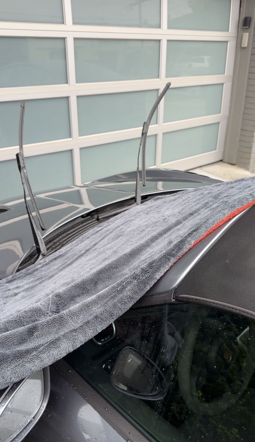 Microfibre towel drying the windscreen cowl of a Porsche 718 Spyder RS with the wipers lifted.