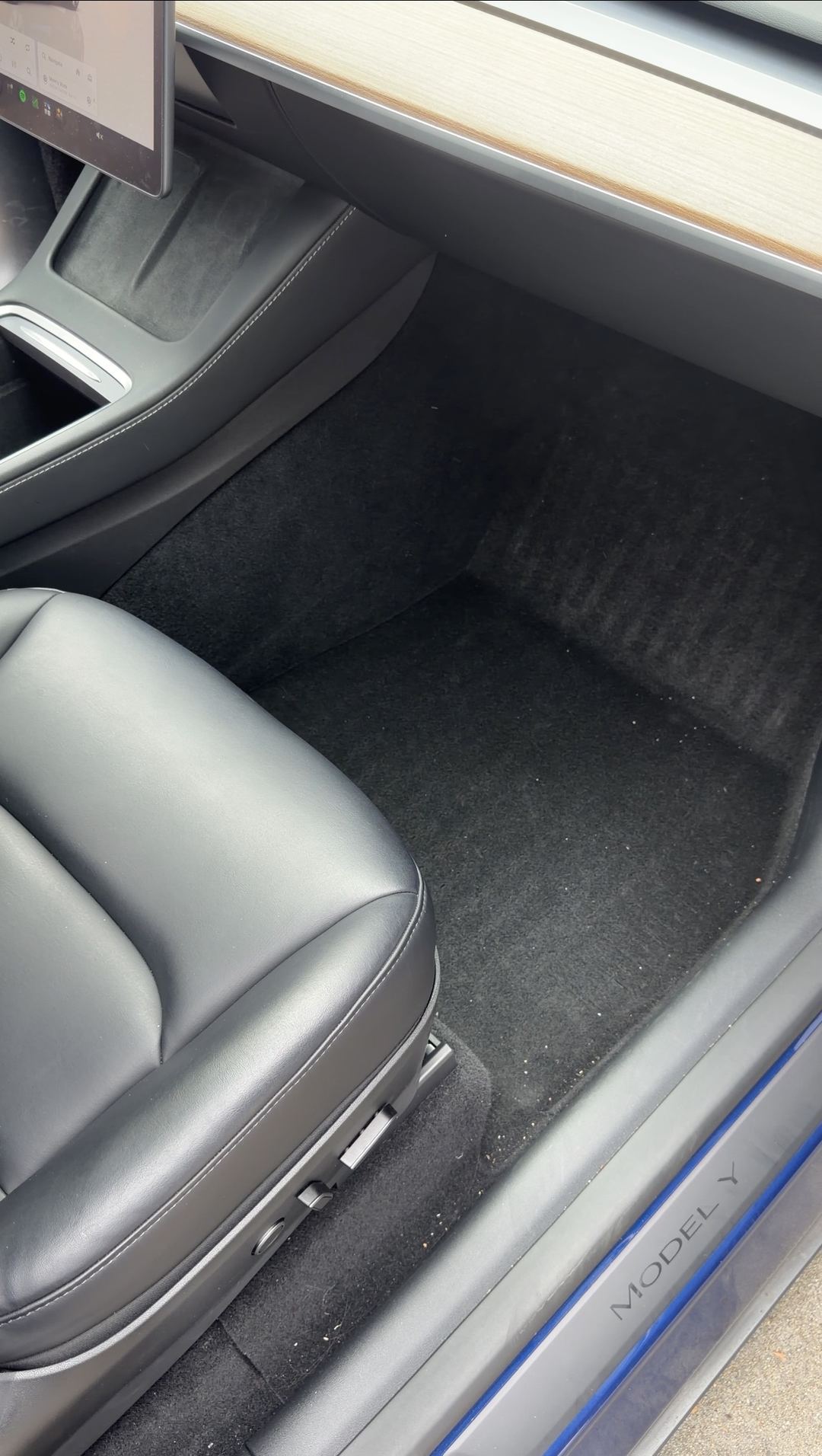 Front passenger footwell of a Tesla Model Y with the floor liner removed, carpet exposed before cleaning.
