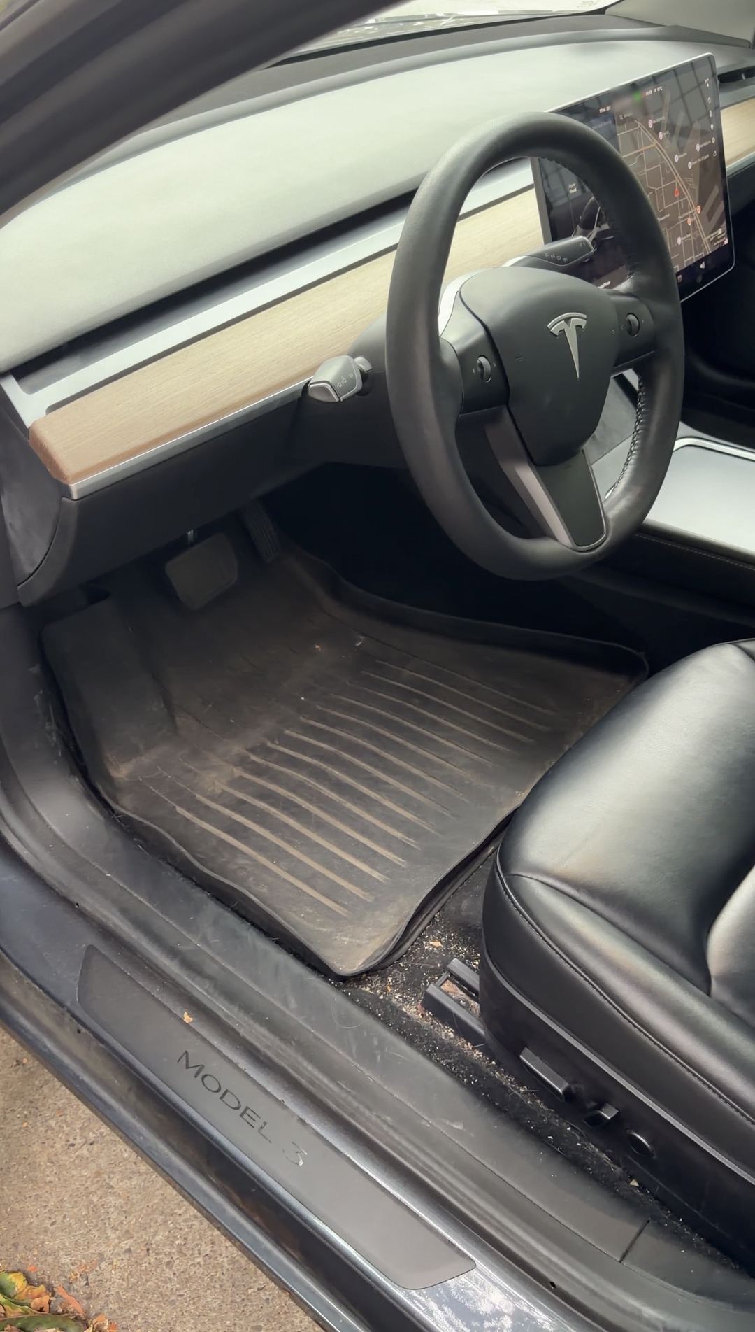 Tesla Model 3 driver footwell before cleaning, dusty rubber mat and debris by the seat rail