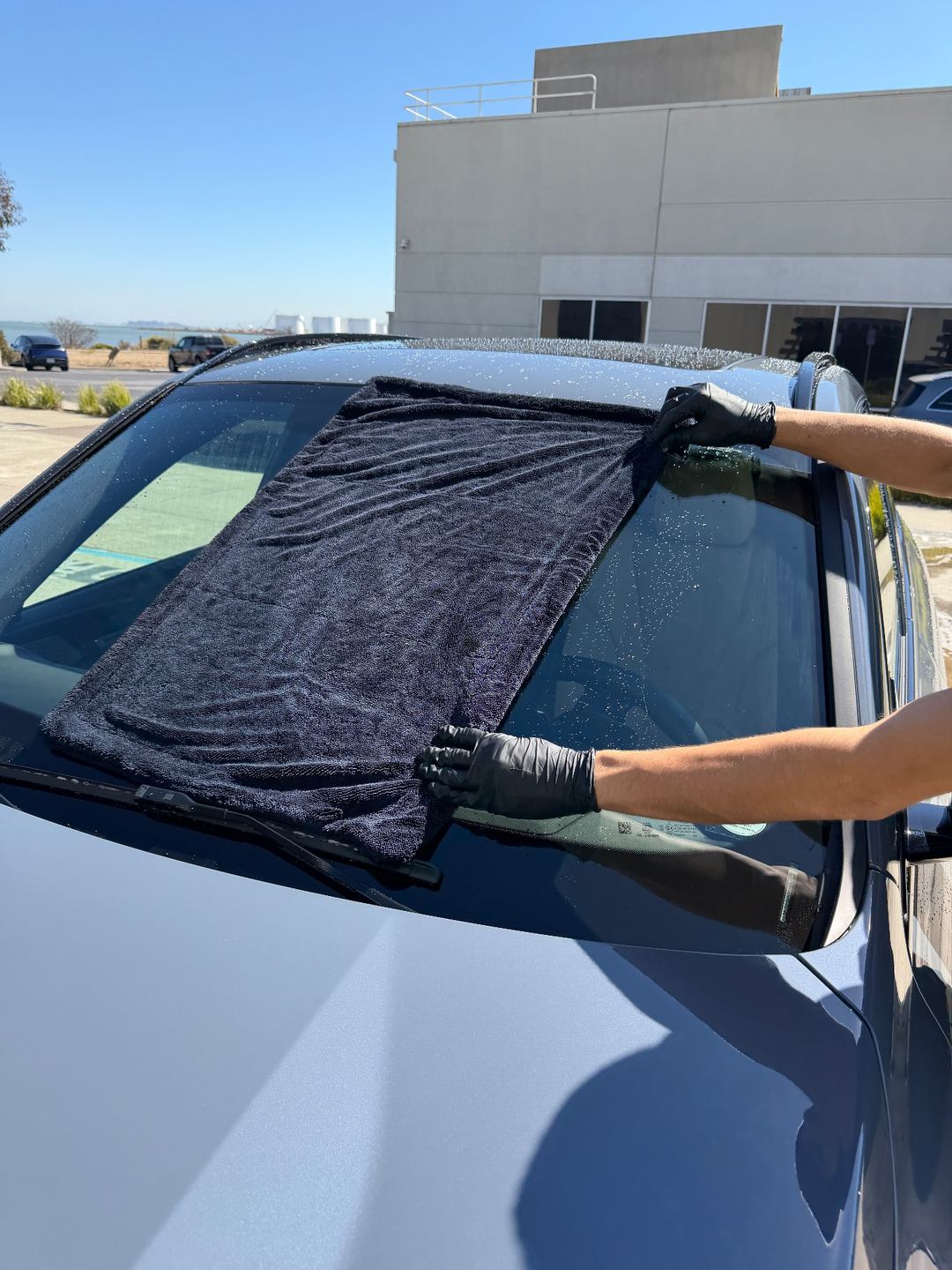 Drying the windshield of a grey BMW X1 with a microfibre towel