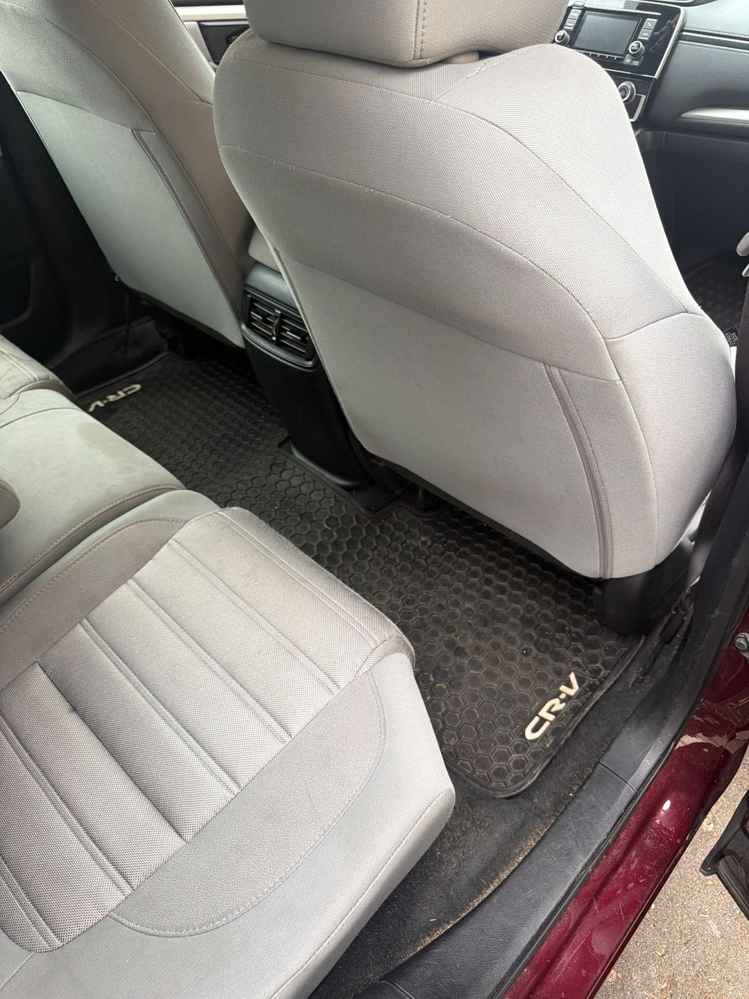 Rear passenger-side footwell of a maroon Honda CR-V before detailing, the rubber mat dusty and gritty