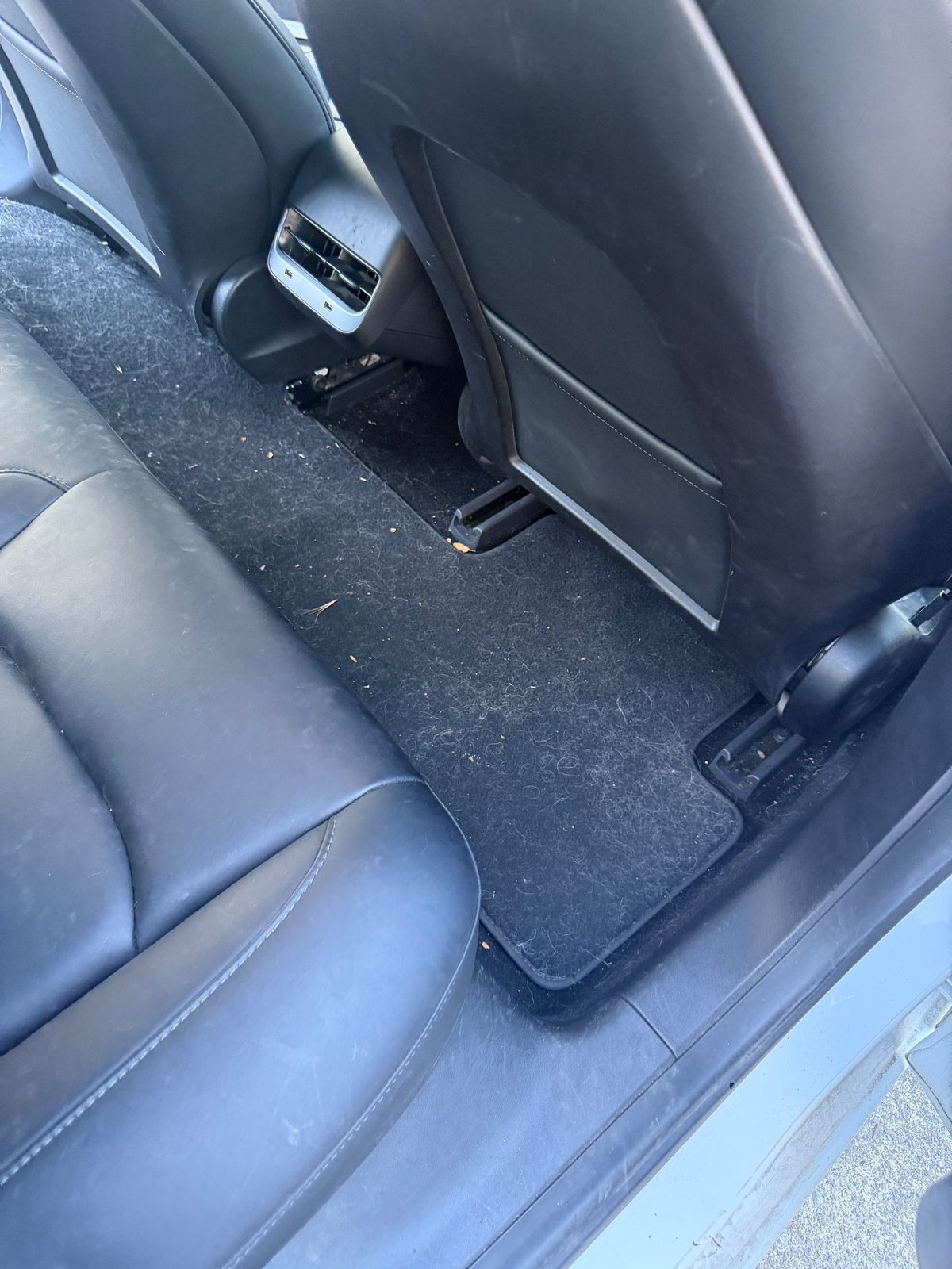 Rear footwell of a white Tesla Model 3 before detailing, with lint and debris on the carpet