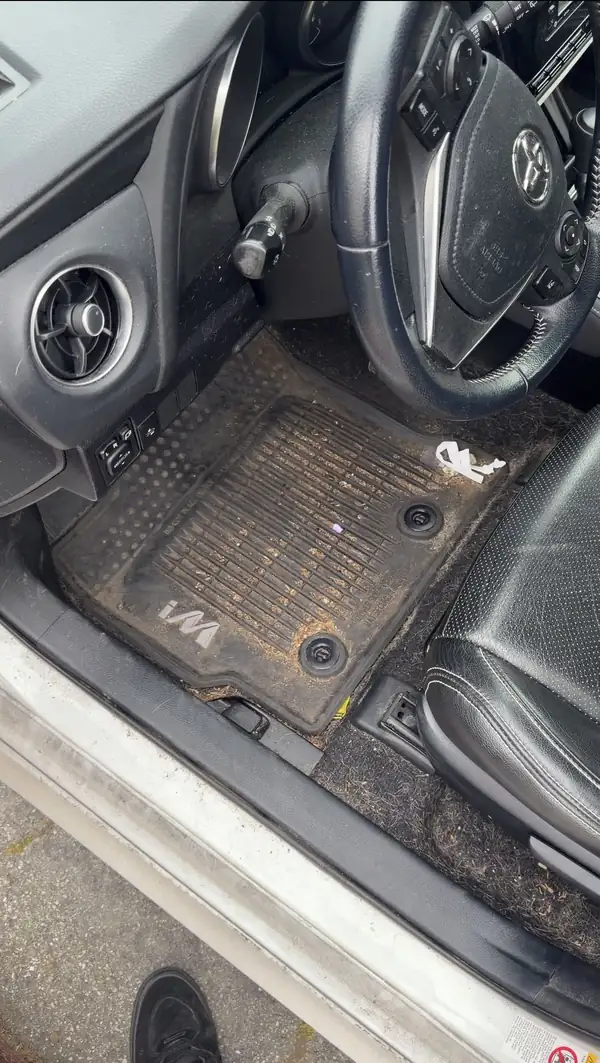 Driver's footwell of a Toyota Corolla iM before detailing, with an iM-branded rubber floor liner caked in brown grit and a dirty door sill.