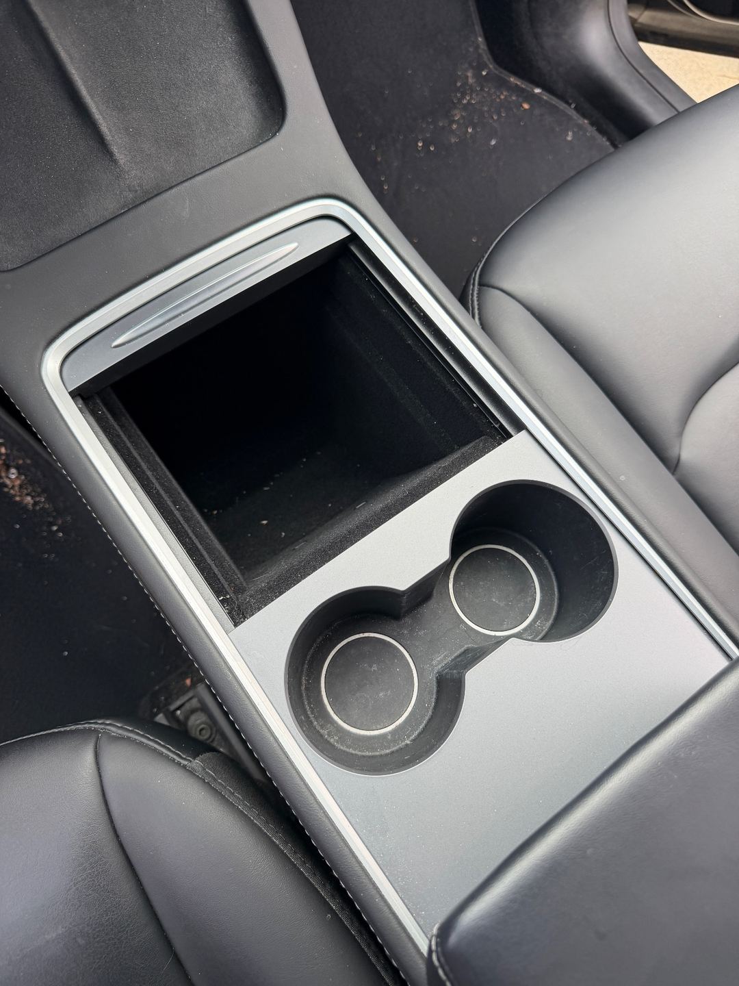 Centre console and cupholders of a Tesla Model Y before detailing, with dust in the cupholders