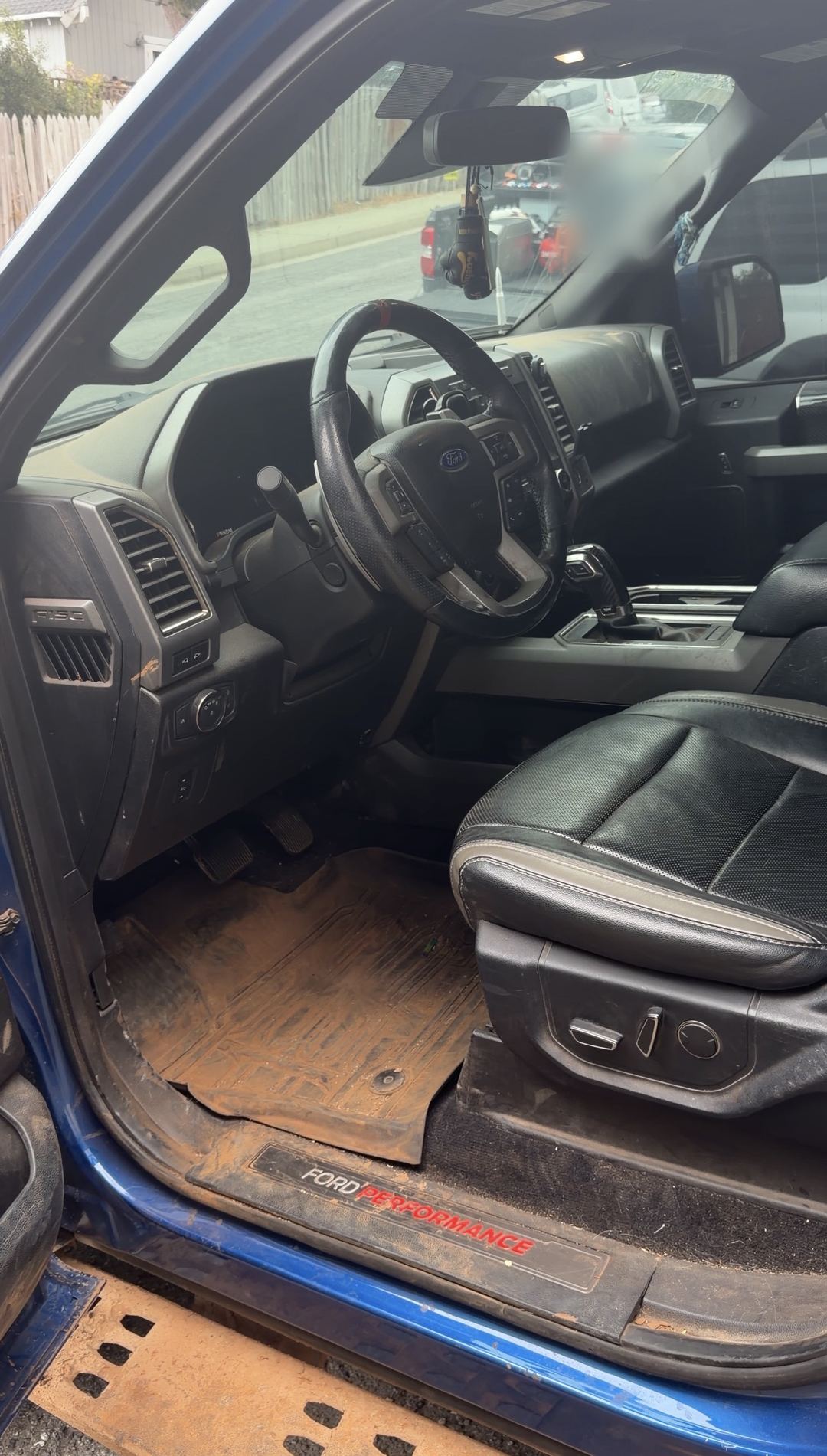 Driver's footwell of a Ford F-150 Raptor with the floor liner caked in dried mud