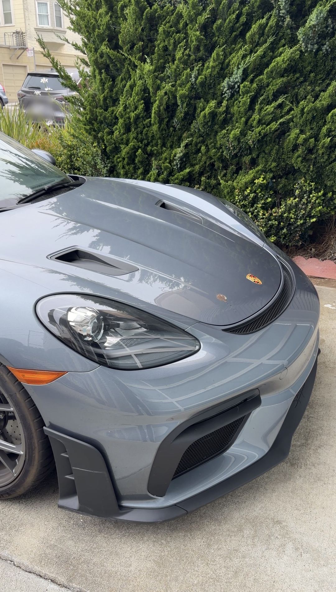Front corner of a grey Porsche 718 Spyder RS before a wash, with a bird dropping on the bonnet next to the Porsche crest.