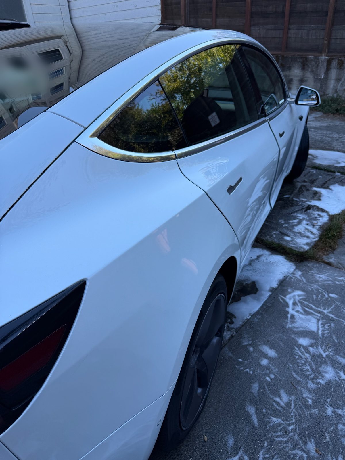 Side of a white Tesla Model 3 after washing, with foam on the pavement