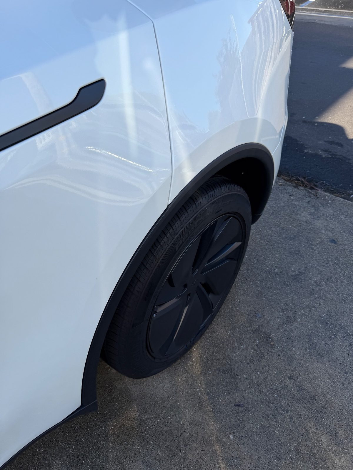 Clean glossy rear quarter and wheel of a white Tesla Model Y after detailing