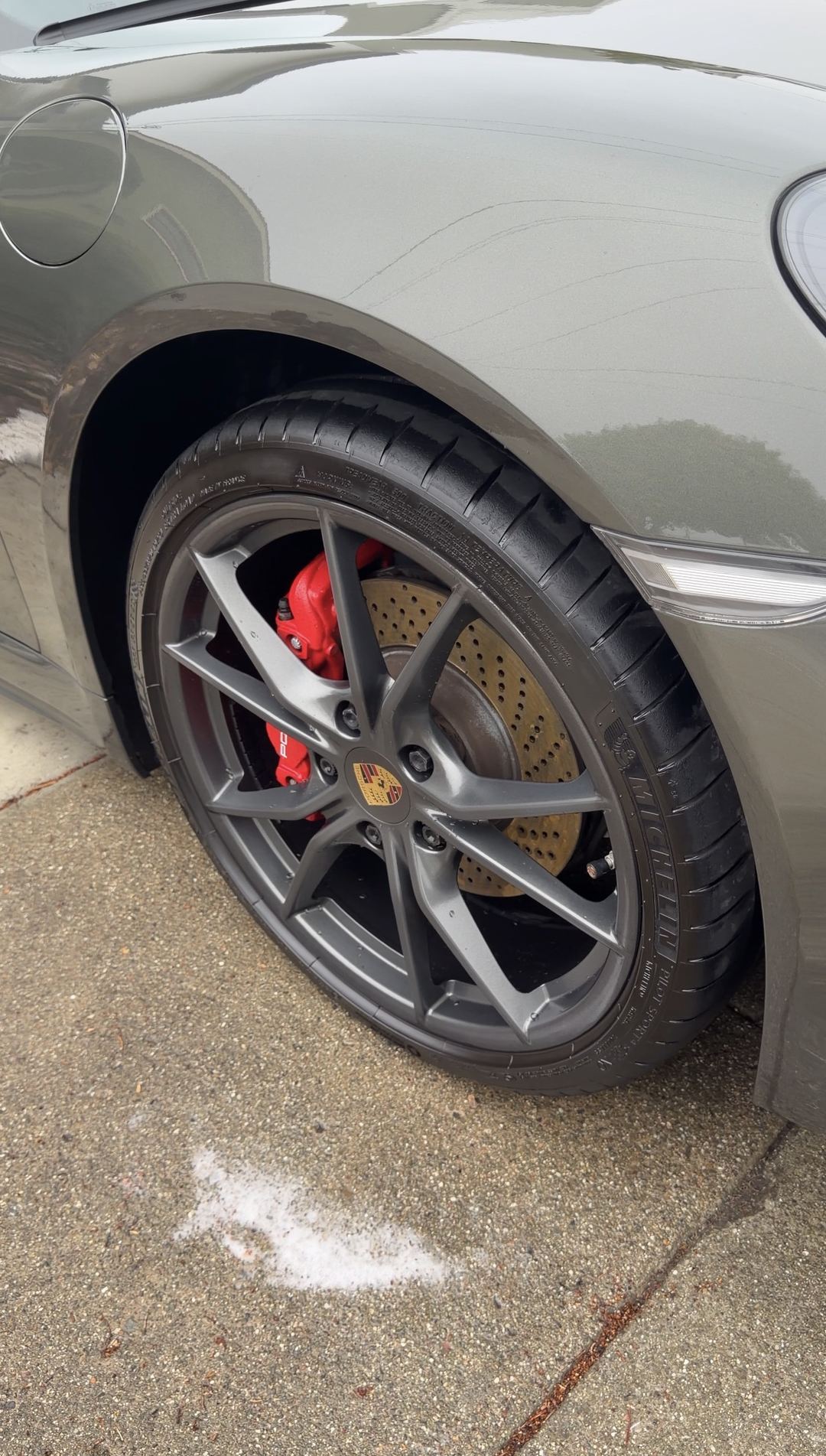 Clean satin silver Porsche wheel with a dressed tyre and red caliper after a mobile detail.