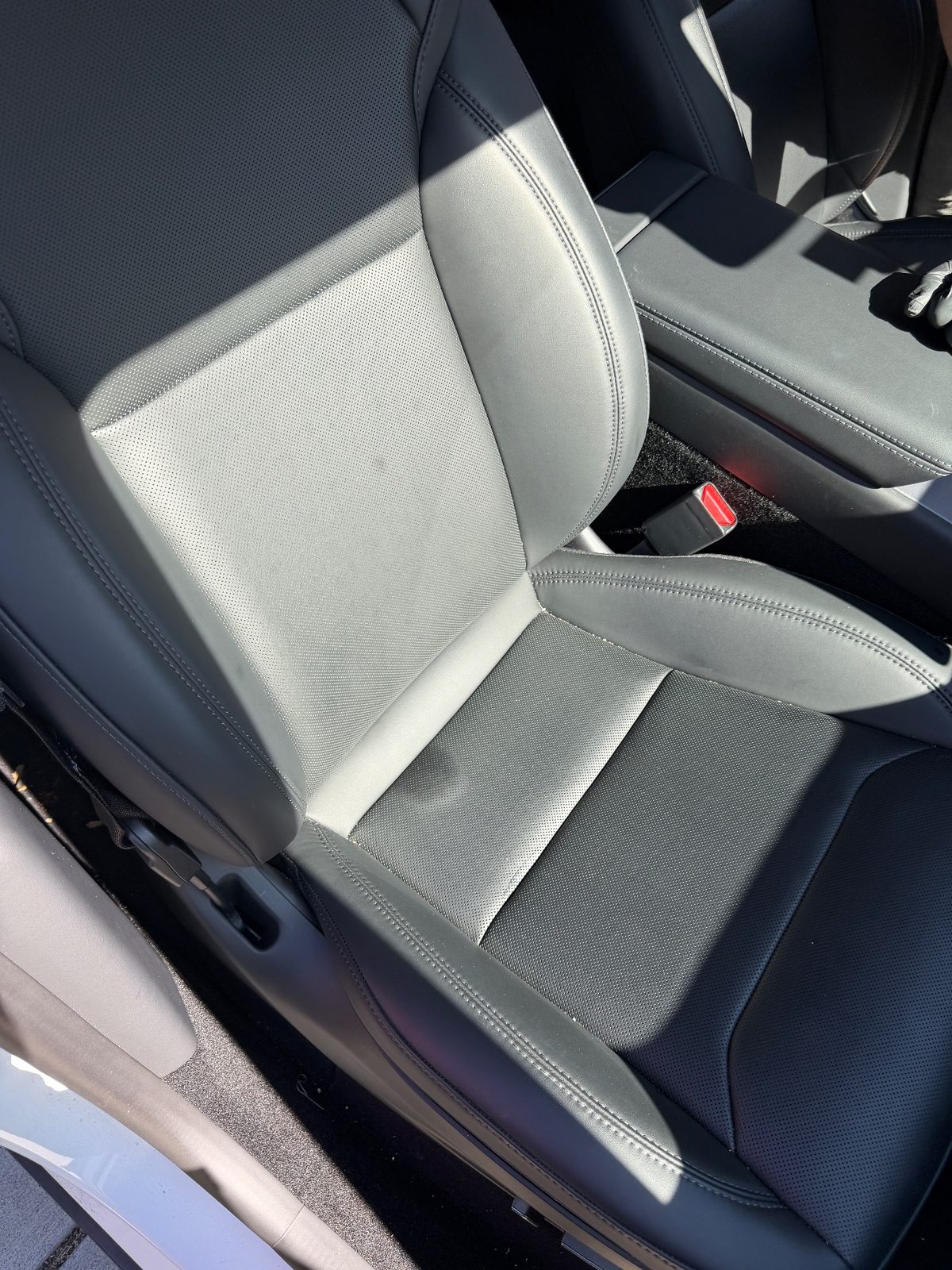 Front passenger leather seat of a white Tesla Model Y before cleaning, dark spots and dust