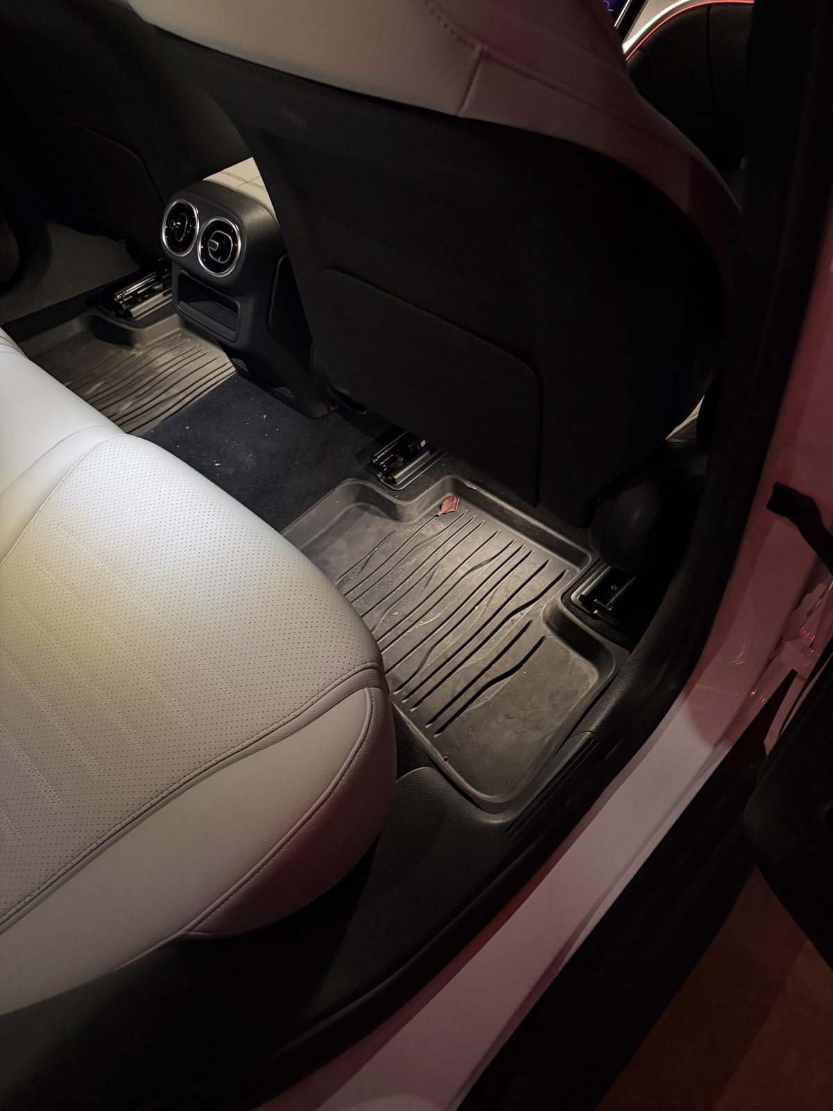 Rear footwell of a white Mercedes GLC before detailing, rubber mat with a leaf, grit and dust