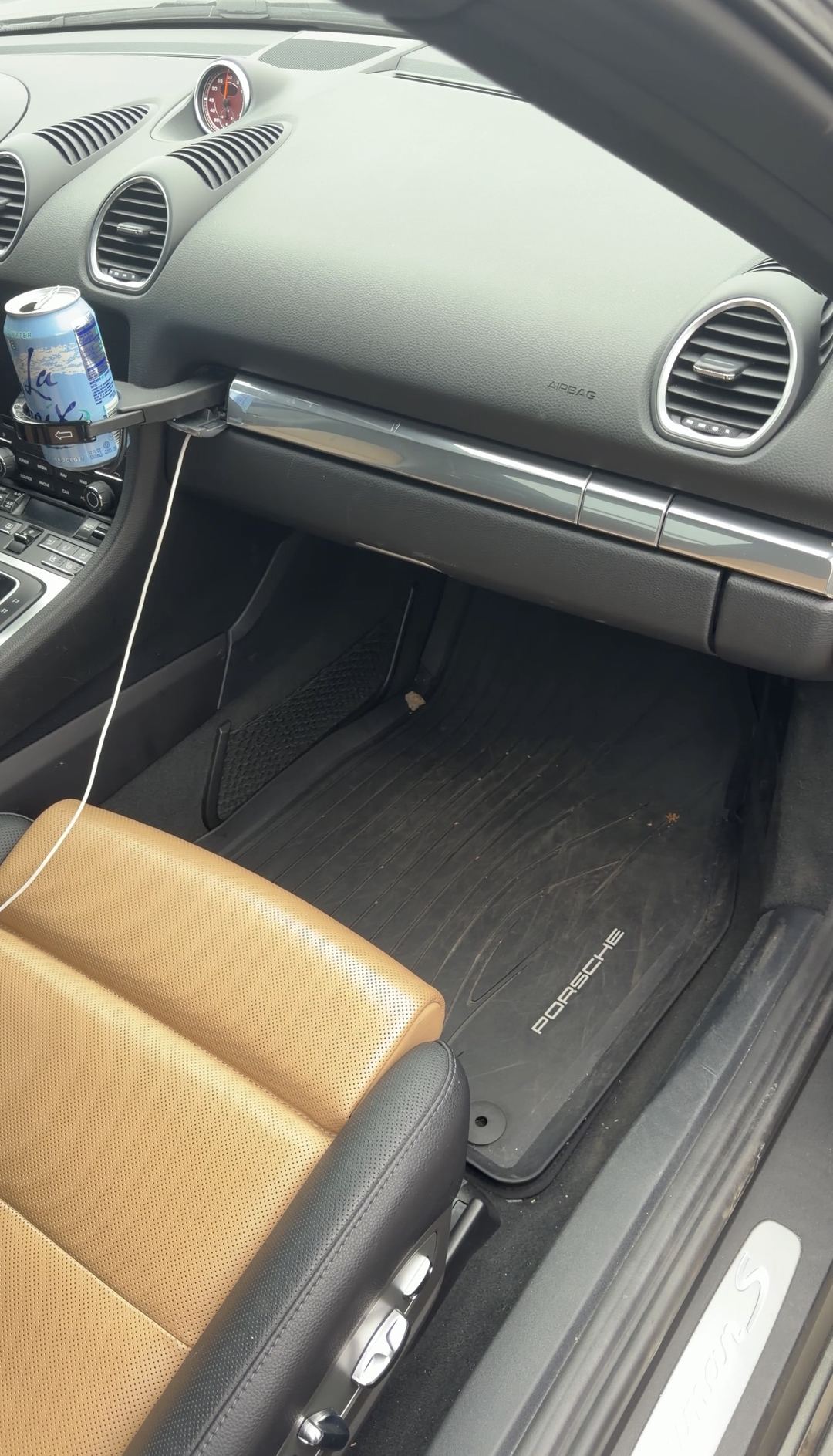 Passenger footwell of a Porsche 718 Cayman S with leaf litter on the floor mat before an interior detail.