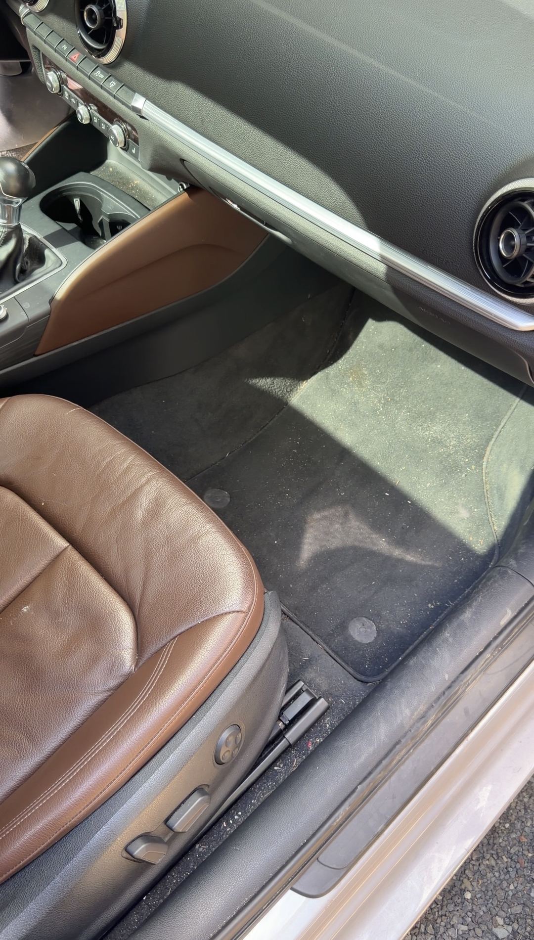 Grit and leaf debris on the front passenger floor mat of a silver Audi A3 with brown leather seats