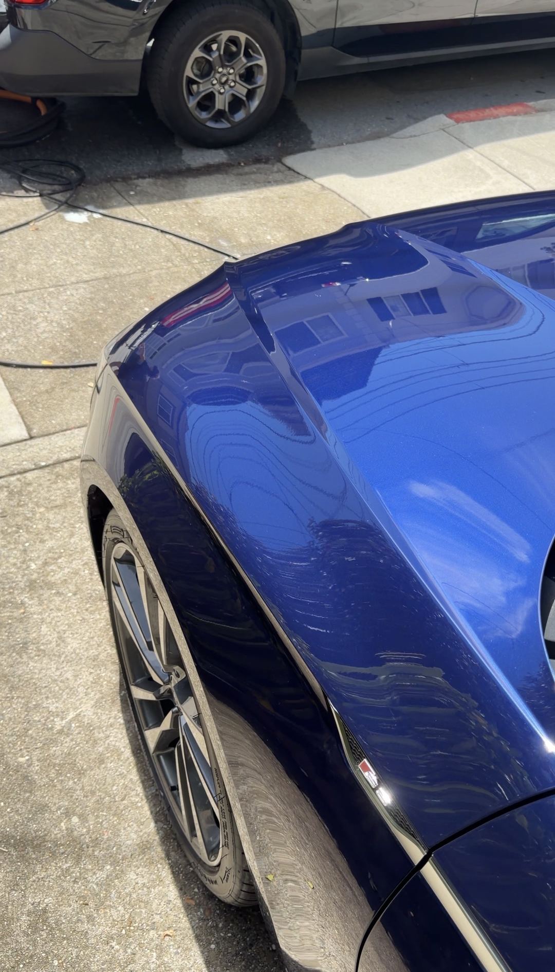 Glossy blue front fender and hood edge of an Audi S5 on a wet driveway