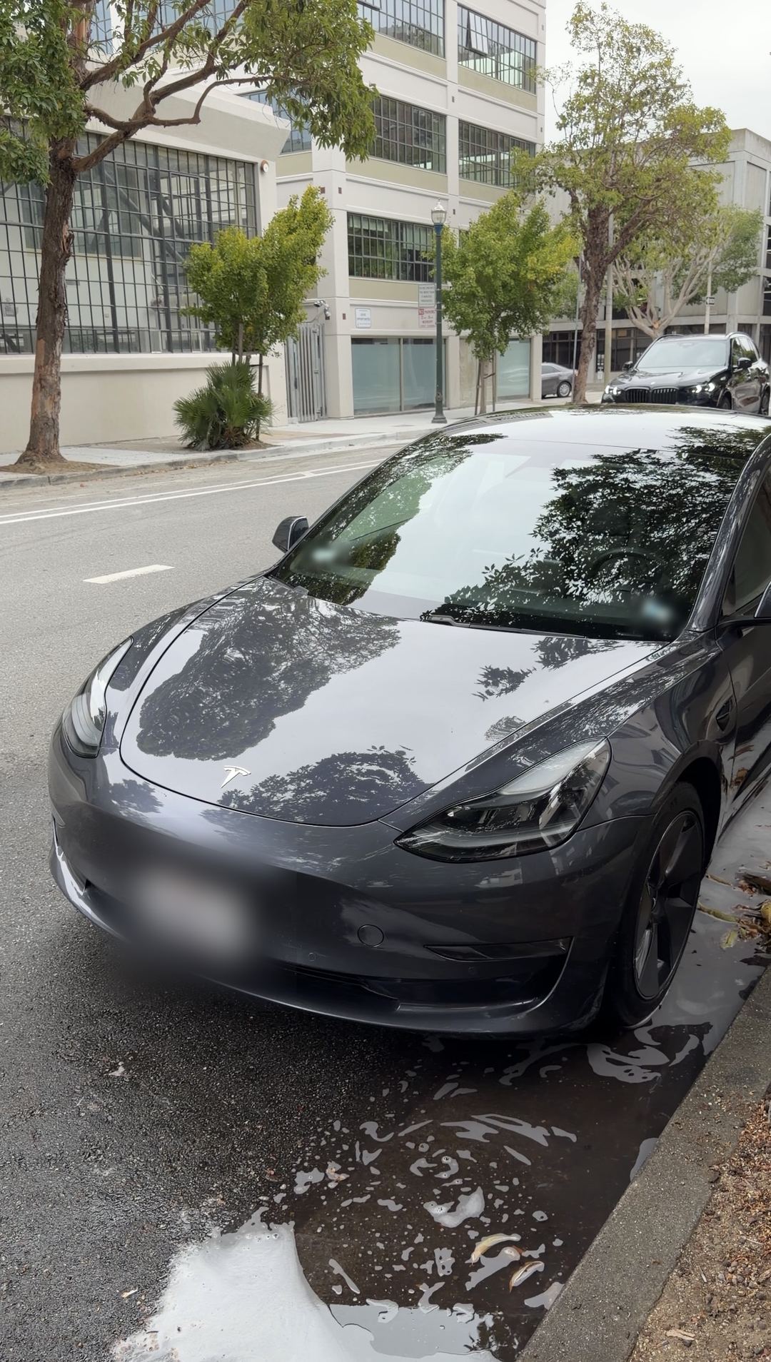 Grey Tesla Model 3 front three-quarter after washing, parked at the curb on a wet street