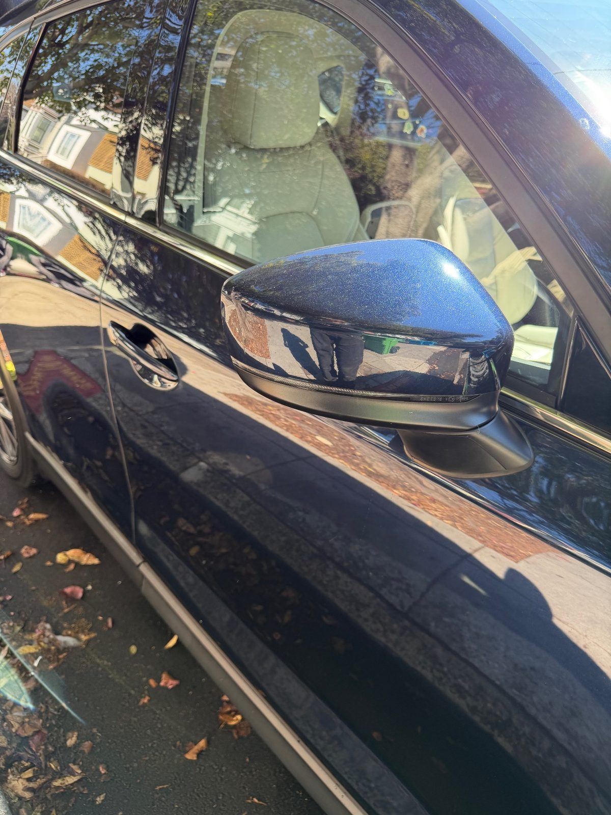 Passenger door and mirror of a dark blue Mazda CX-5 after washing, glossy paint with street reflections