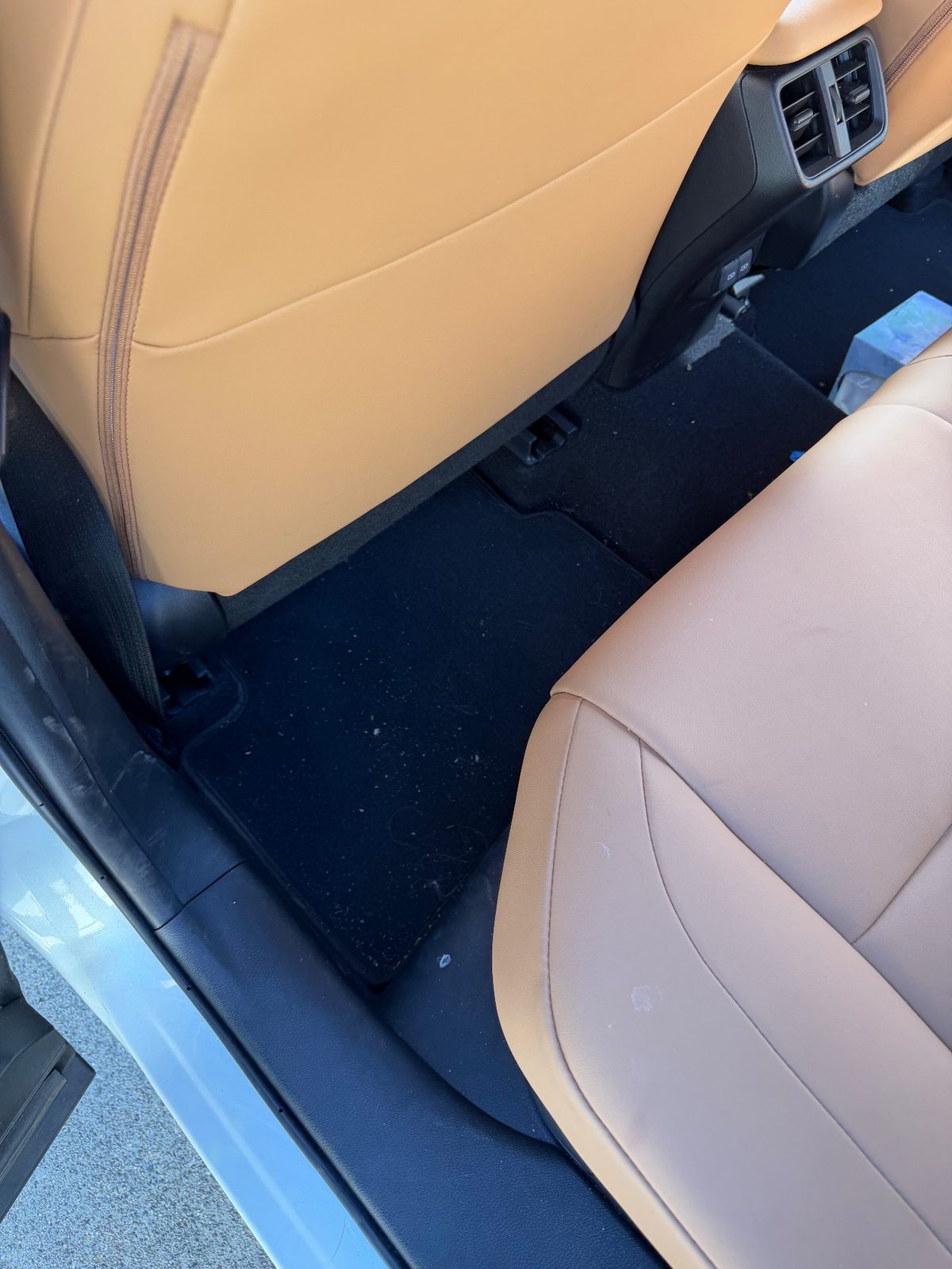 Rear footwell of a white Lexus UX before detailing with crumbs and hair on the mat