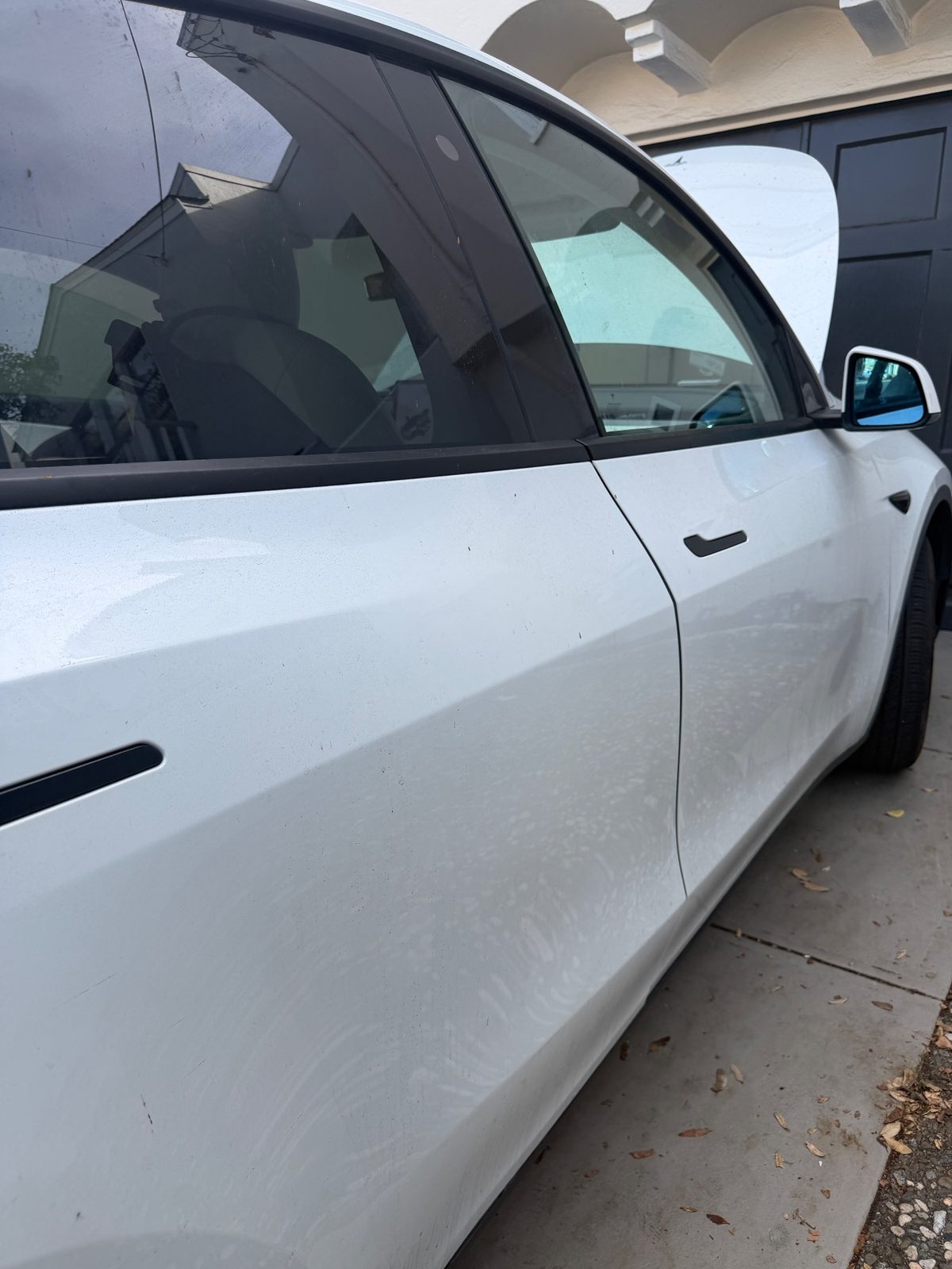 Passenger side of a white Tesla Model Y before detailing, with a dusty film and water spots on the doors