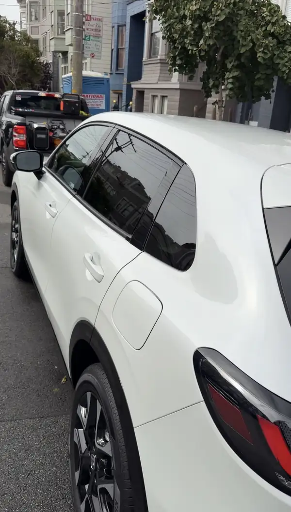 Rear three-quarter view of a white Honda HR-V after detailing, parked on a hilly city street with glossy paint reflecting the sky and overhead wires.
