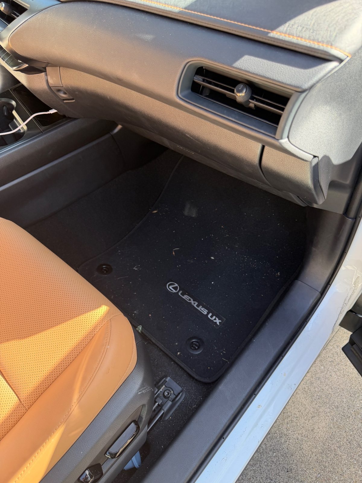 Passenger footwell of a white Lexus UX before detailing, mat covered in crumbs and leaf bits
