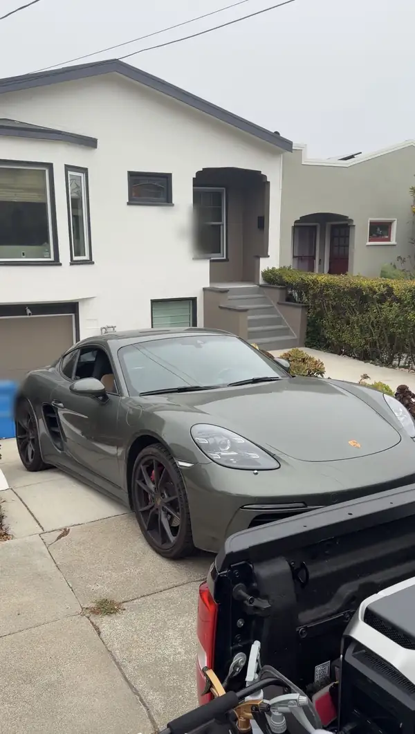 Green Porsche 718 Cayman S parked on a San Francisco driveway before a mobile detail, its paint covered in a dry dust film.