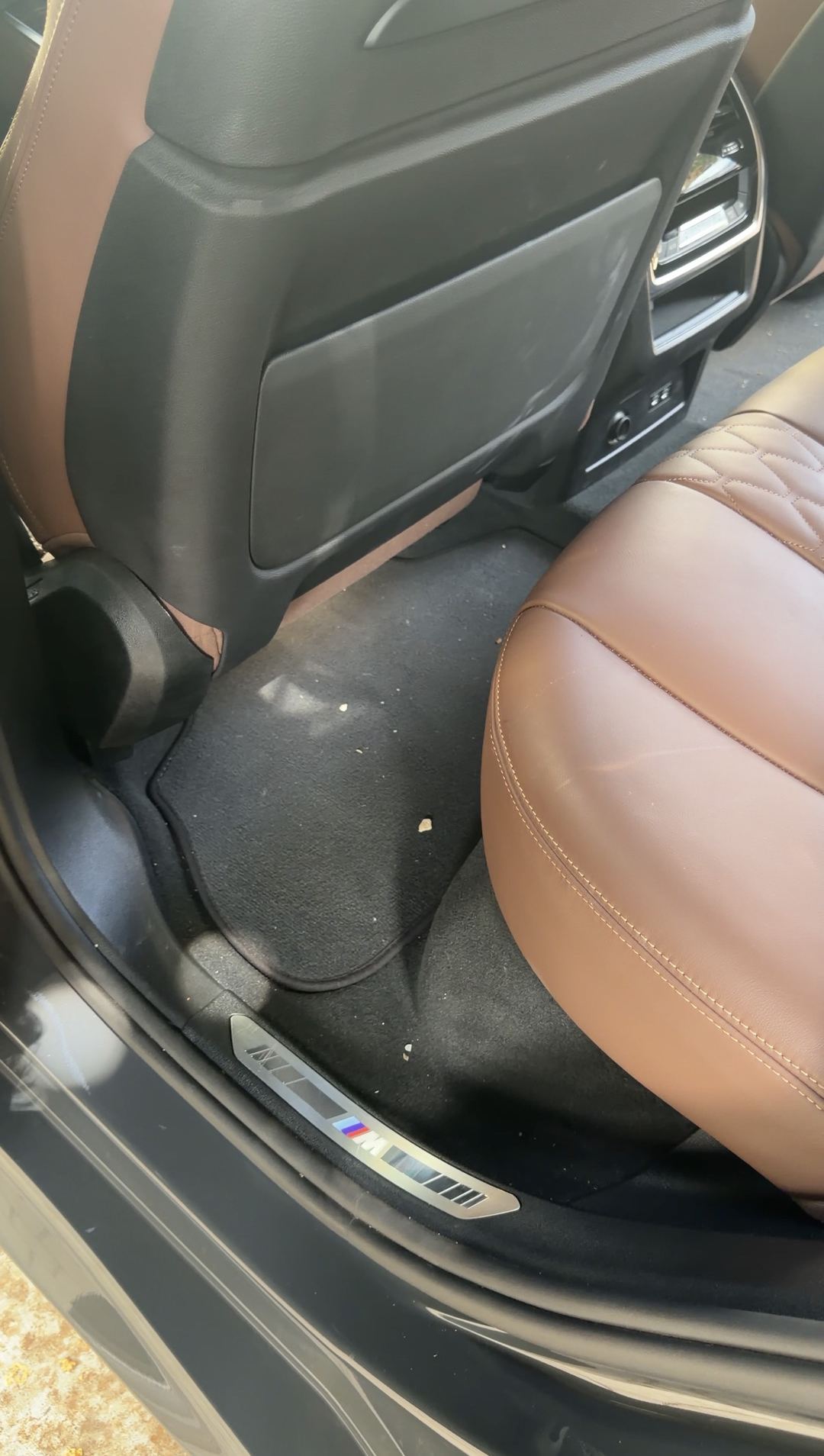 Rear driver-side footwell of a BMW X5 before vacuuming, with crumbs on the floor mat