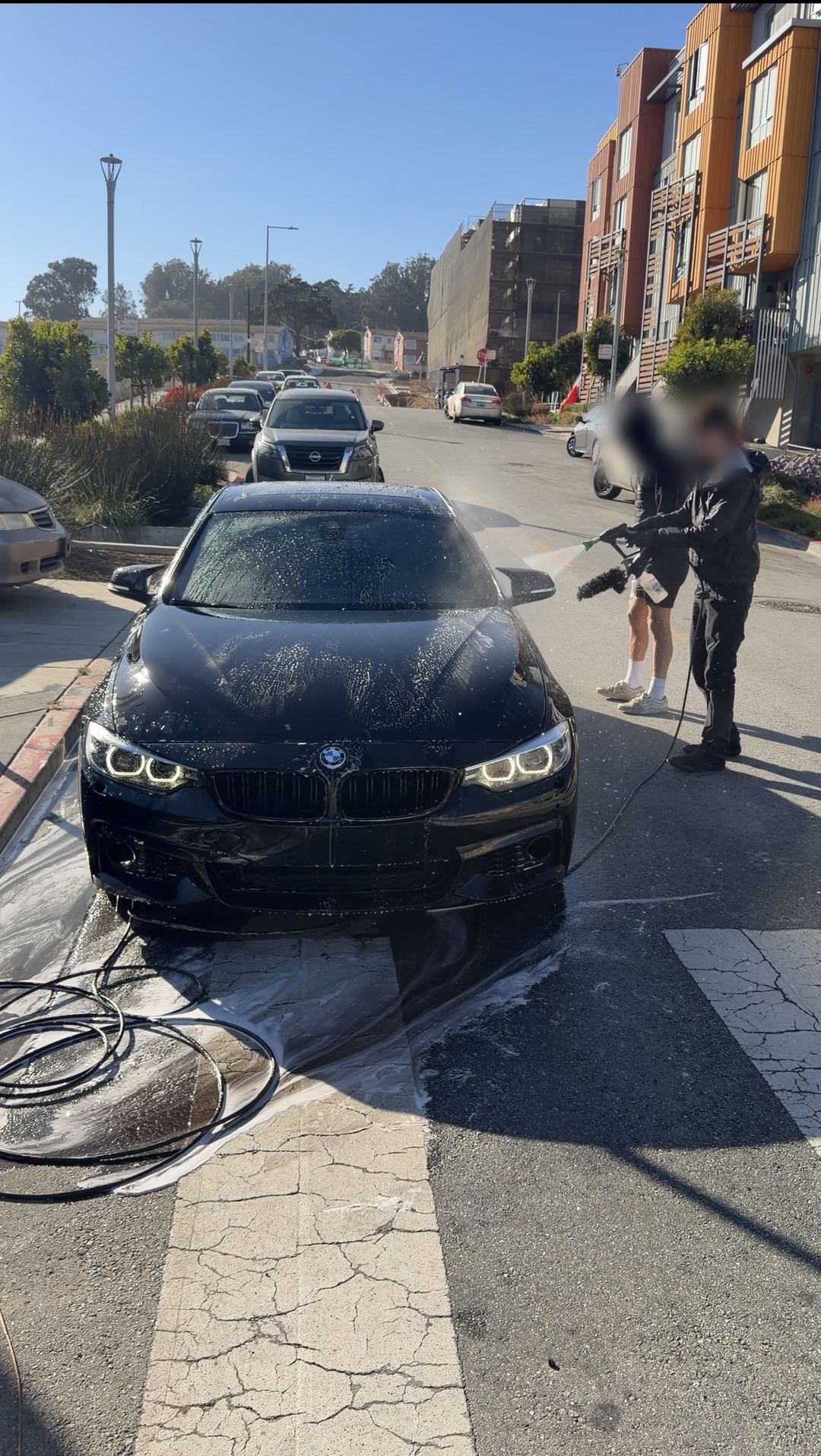 Black BMW 4 Series Gran Coupe being pressure-washed on a San Francisco street during a mobile detail.