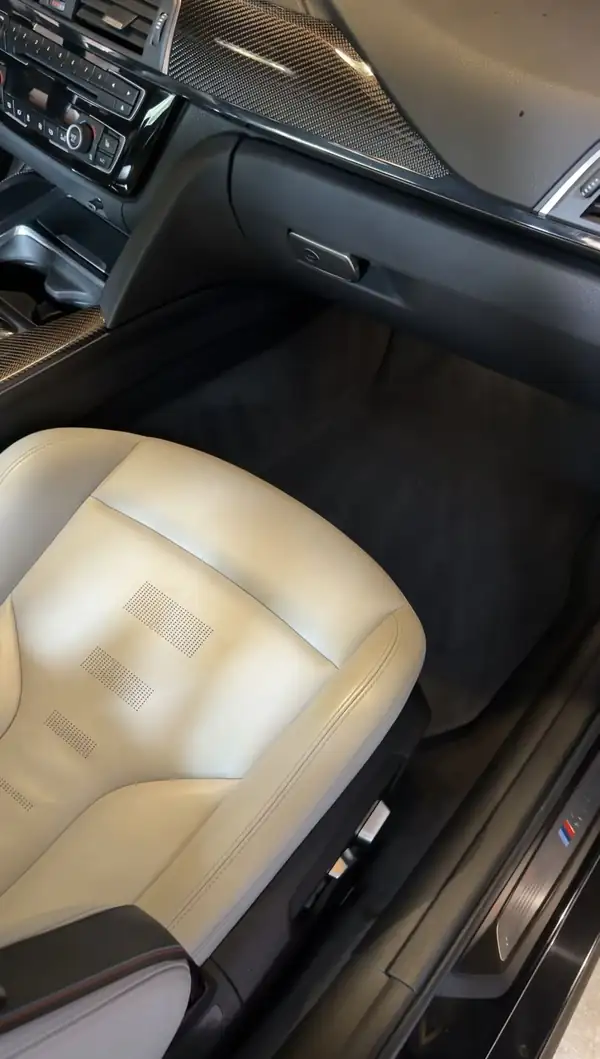 Cleaned passenger footwell of a BMW M3 with a groomed black floor mat and white leather seat