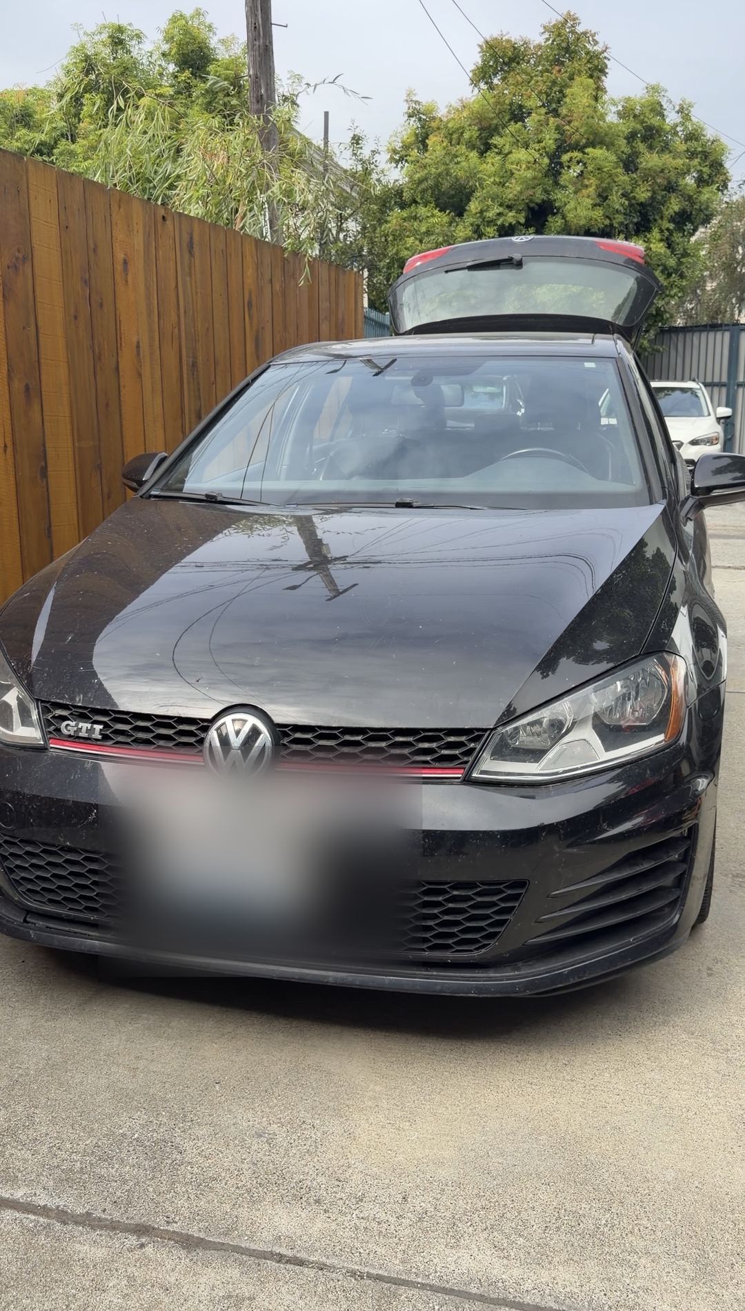 Front of a black VW GTI before washing, parked in a driveway with the hatch open