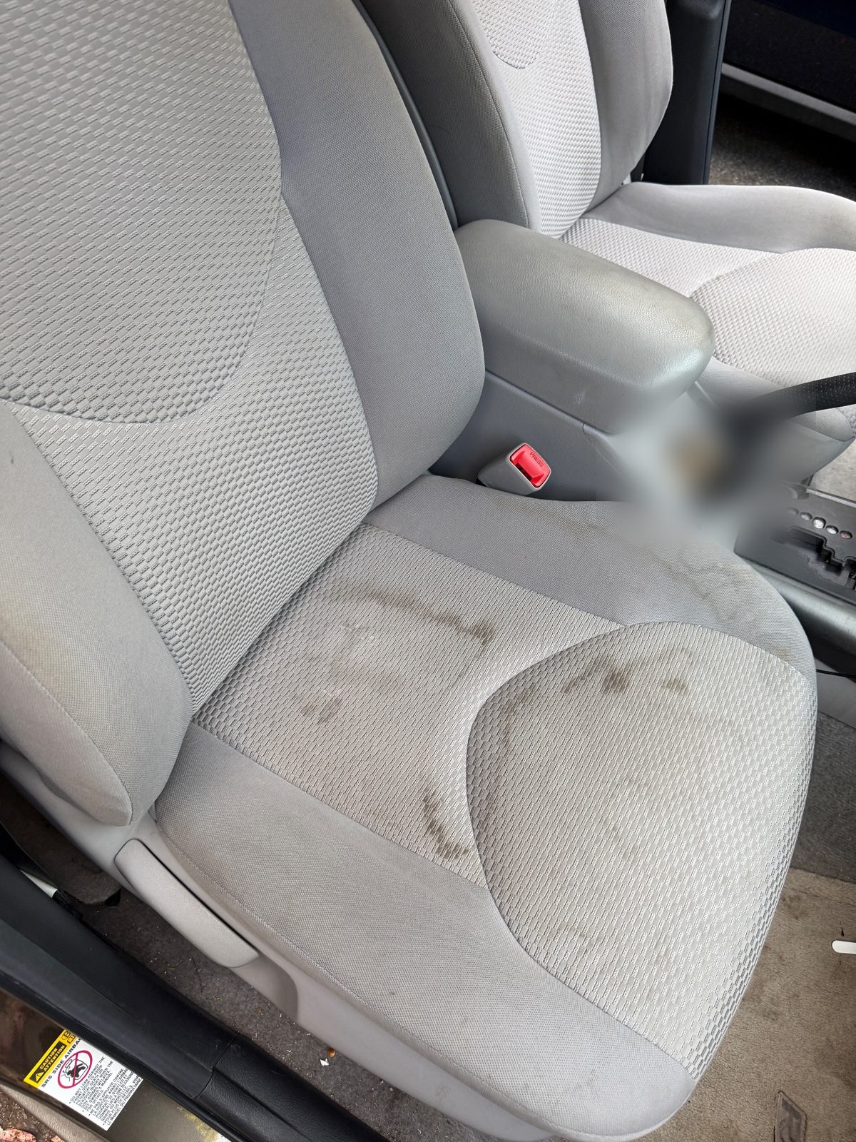 Front cloth seat of a 2011 Toyota RAV4 before detailing, dark liquid stains across the cushion